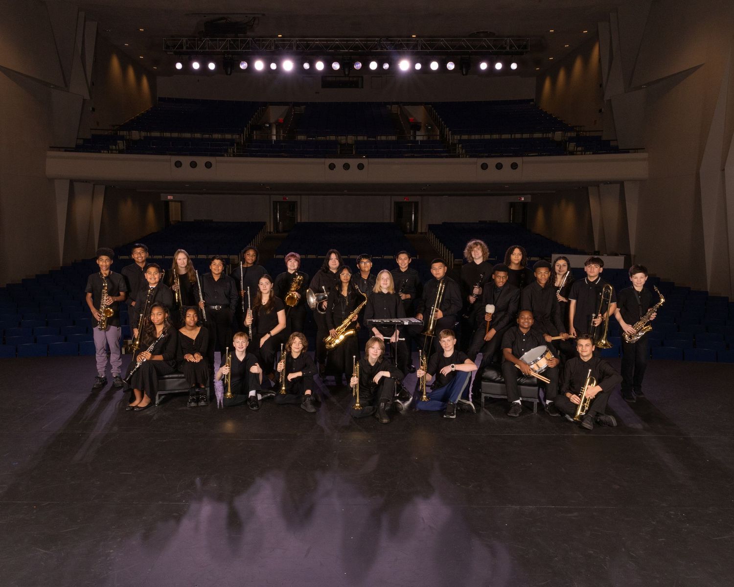 Group of performers dressed in black seated on stage in dramatic lighting for a formal performance.