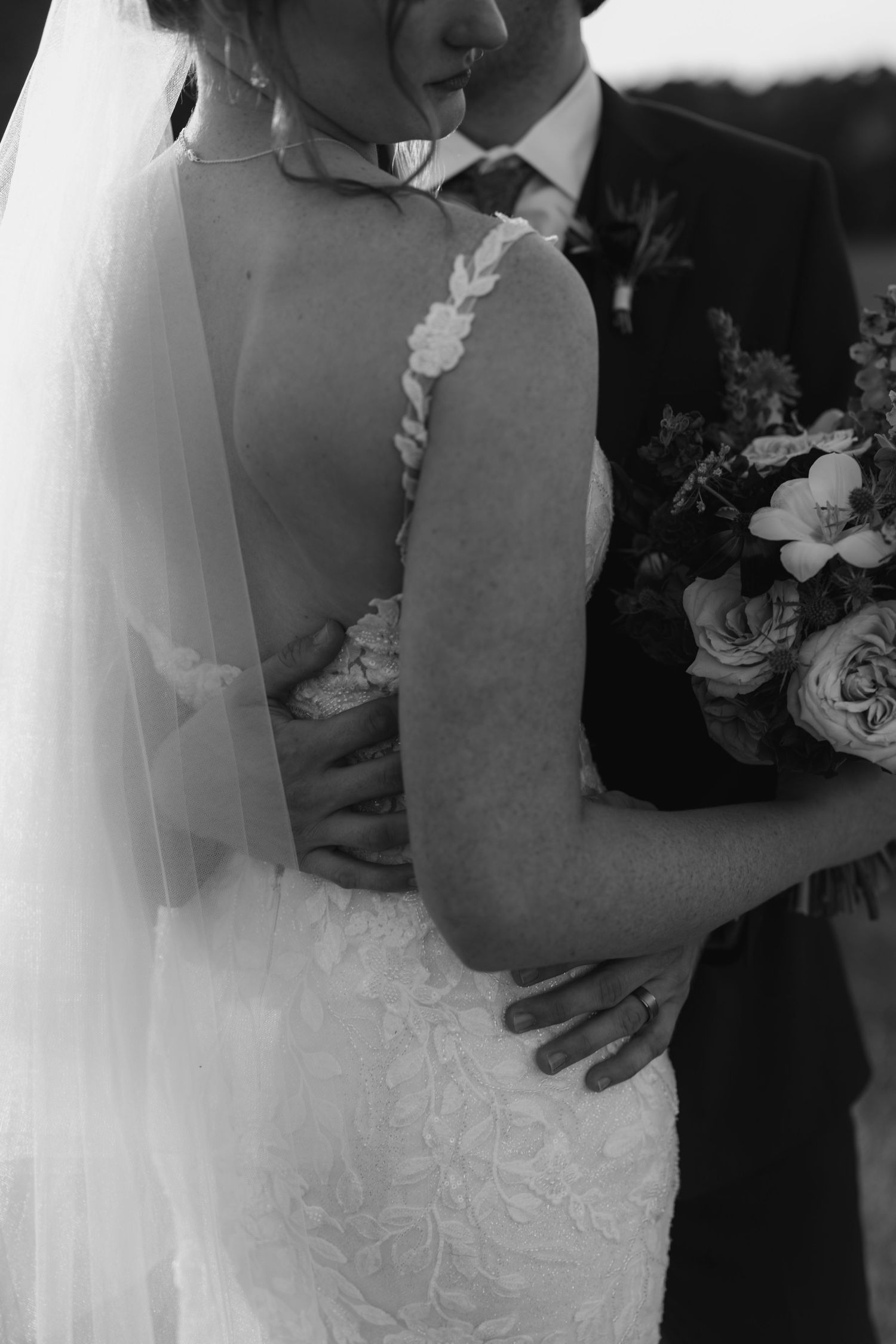A close-up black and white photo of a bride and groom embracing during their wedding ceremony.
