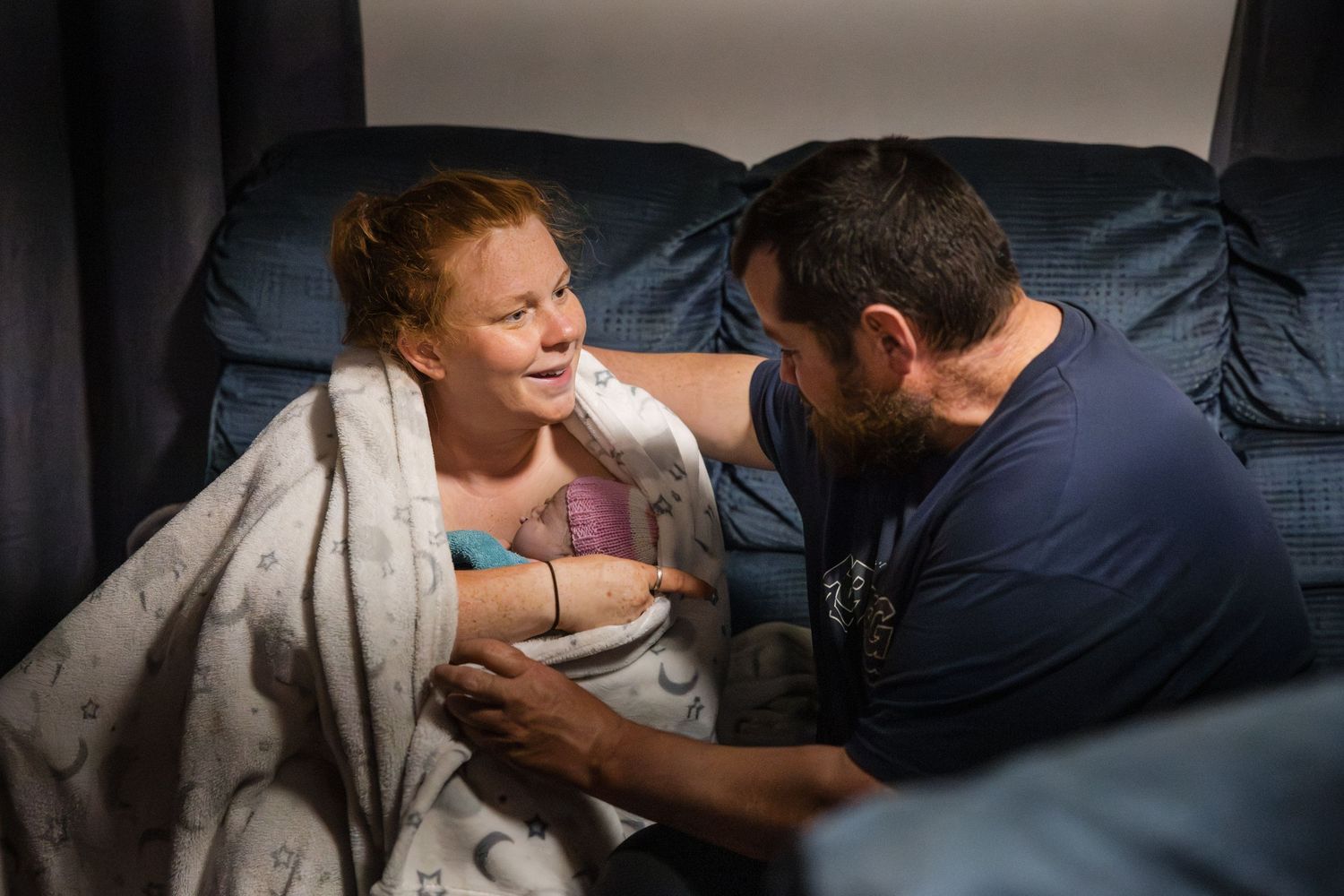People resting together on a couch or bed in low-light conditions with soft ambient lighting.