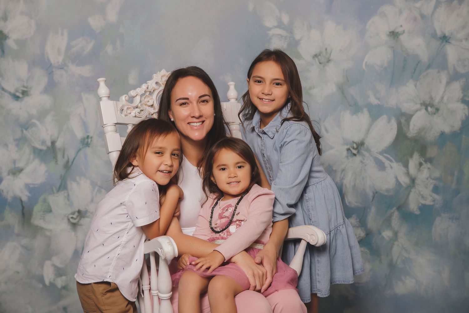 Four children in coordinated pastel outfits pose together against a soft floral backdrop for a portrait session.