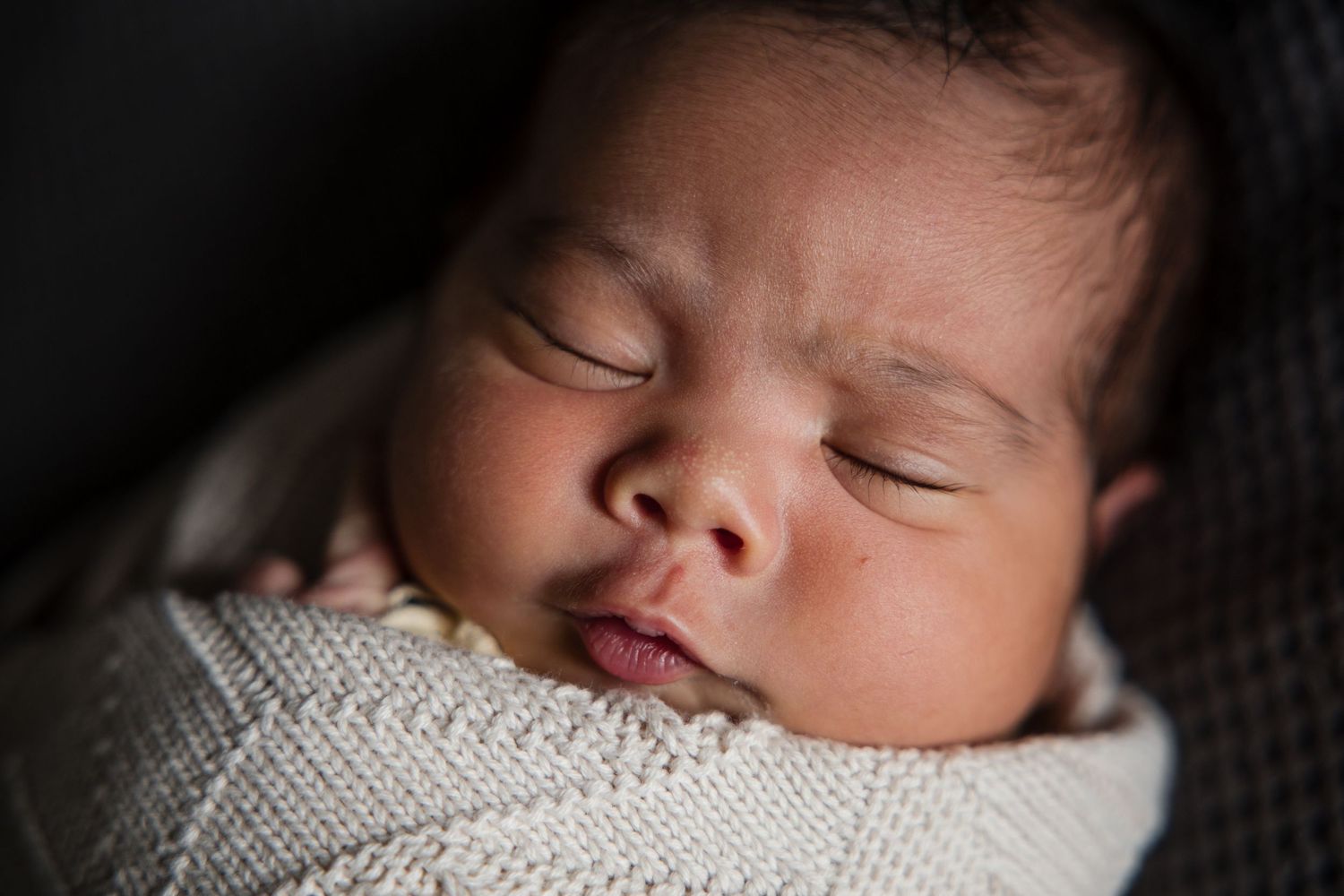 Peaceful newborn baby sleeping soundly wrapped in a soft cream knit blanket, close-up portrait photography.