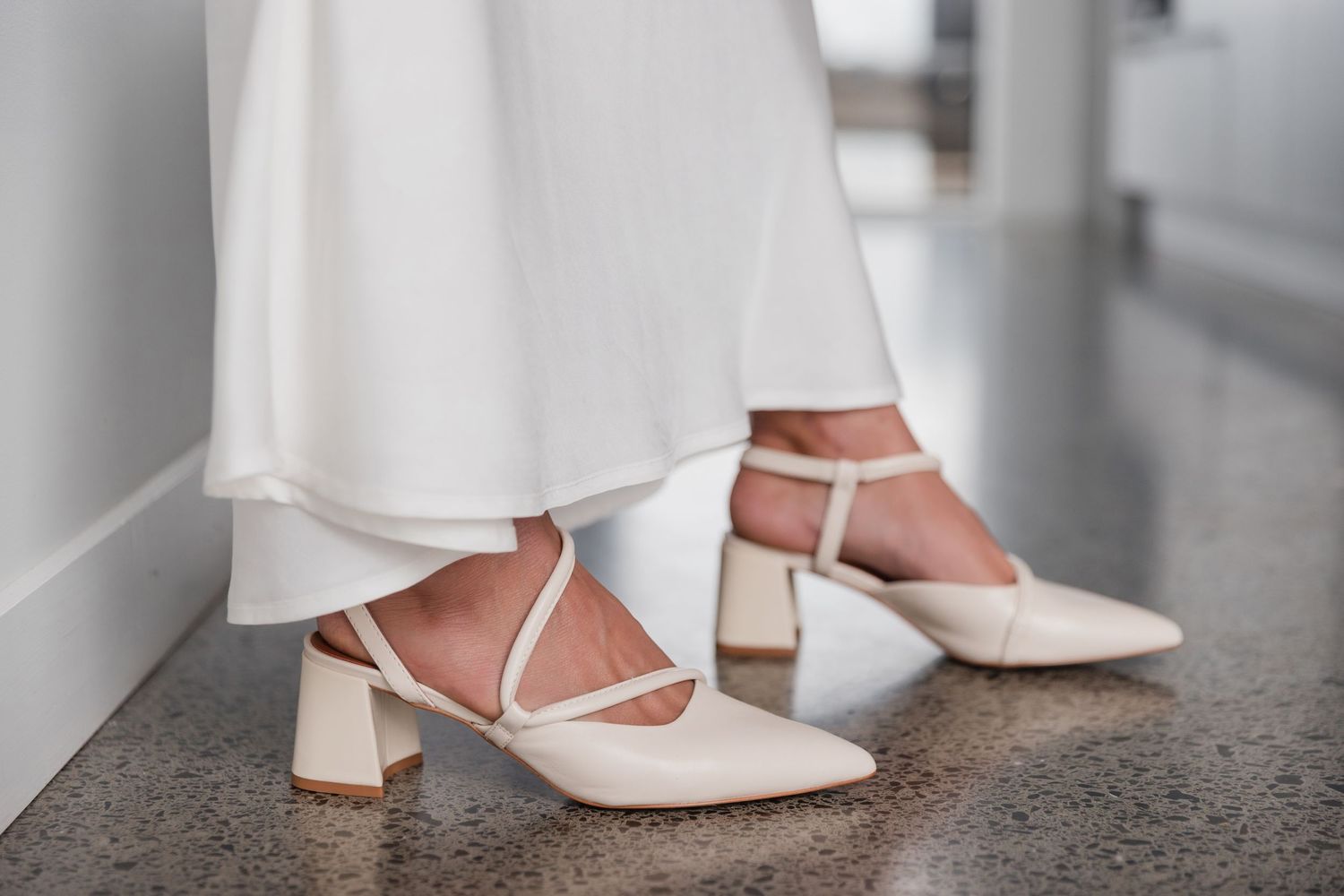 Close-up view of white wedding dresses and shoes as people walk in line during a formal ceremony.