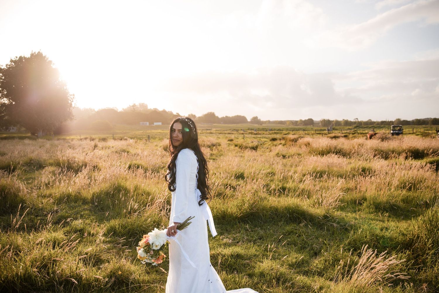 White dress in flowing motion against sunset-lit field of tall grass and distant trees.