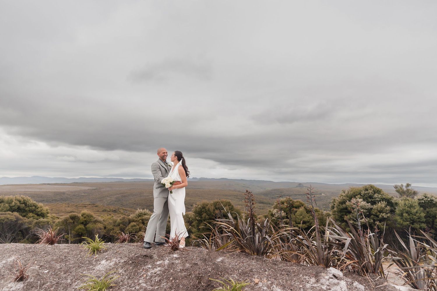 Couple sharing an intimate moment on a scenic mountain overlook with cloudy skies in the background.