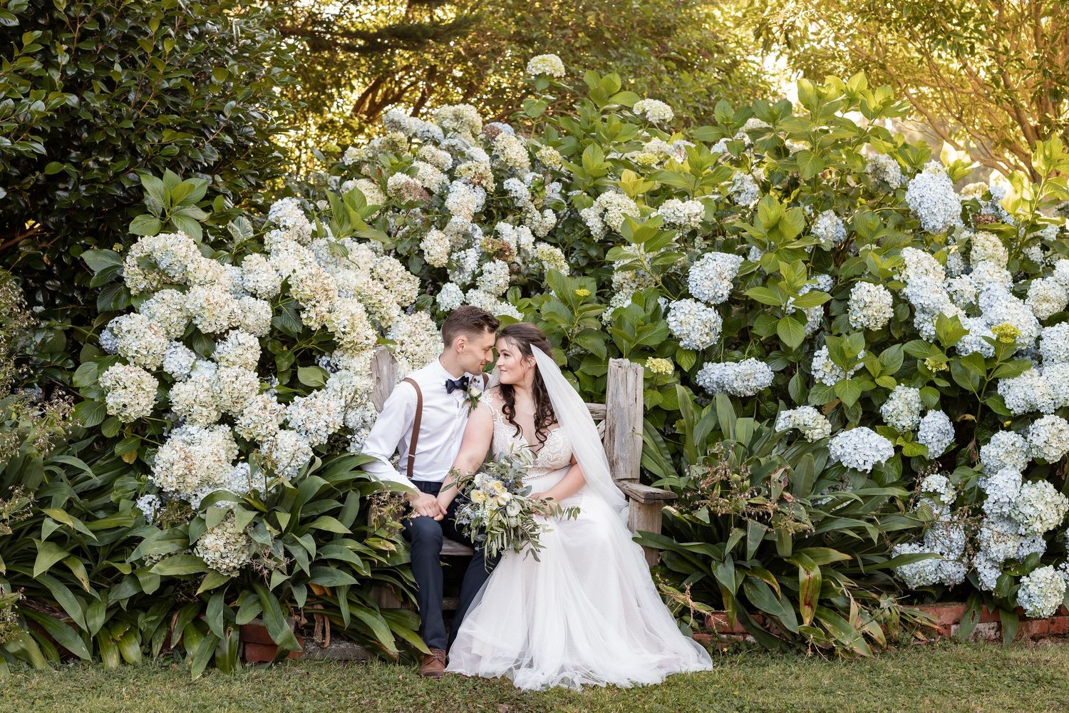 A romantic summer garden wedding photoshoot with white hydrangea bushes creating a beautiful floral backdrop at sunset.