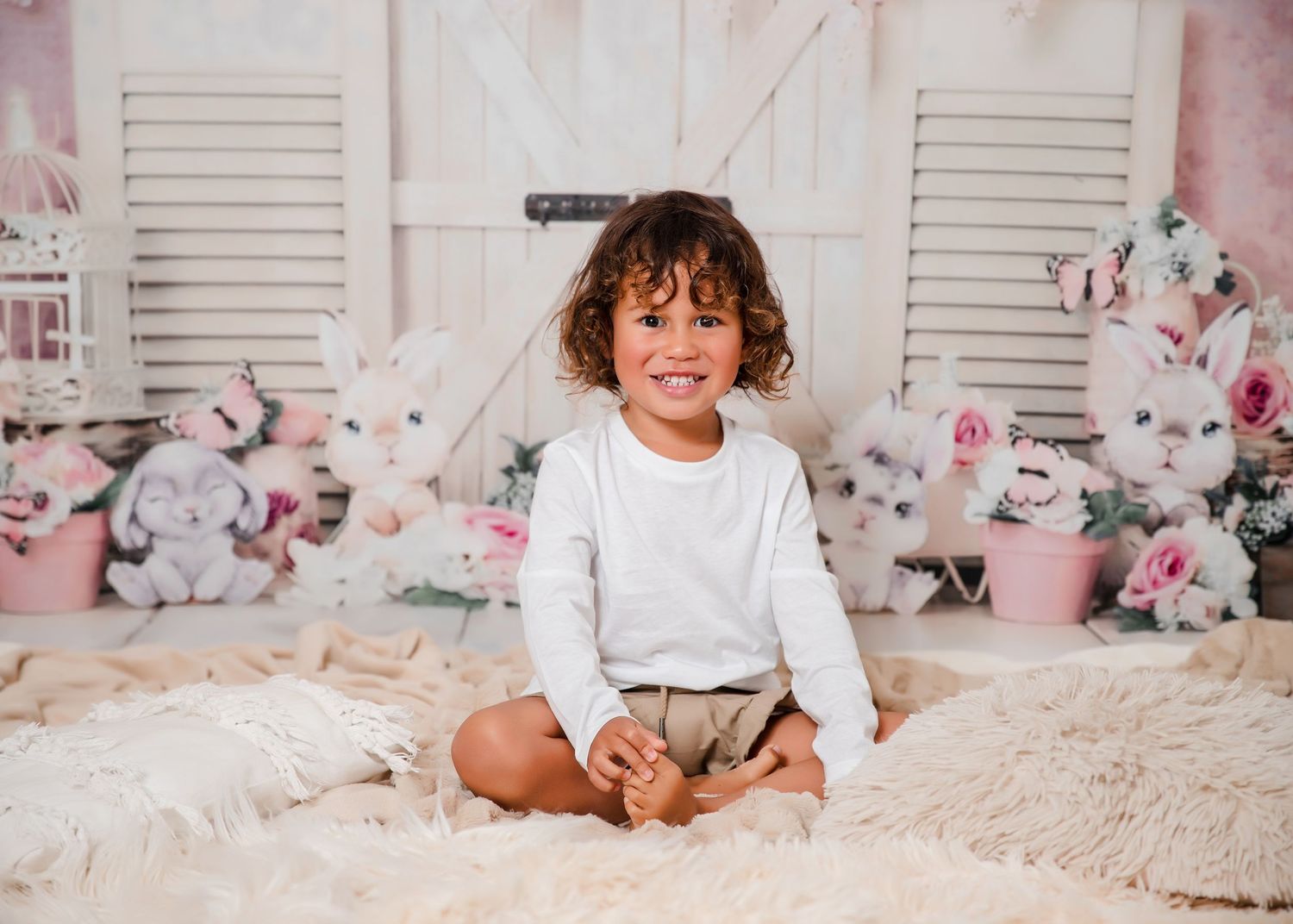 Small child in white shirt sits on cream colored carpet with floral backdrop and white shutters in background.