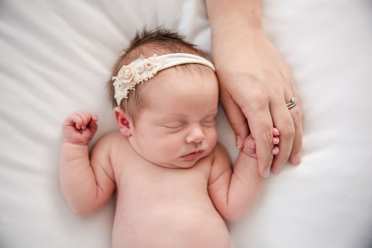Peaceful sleeping newborn baby wearing a delicate lace headband on soft white bedding.