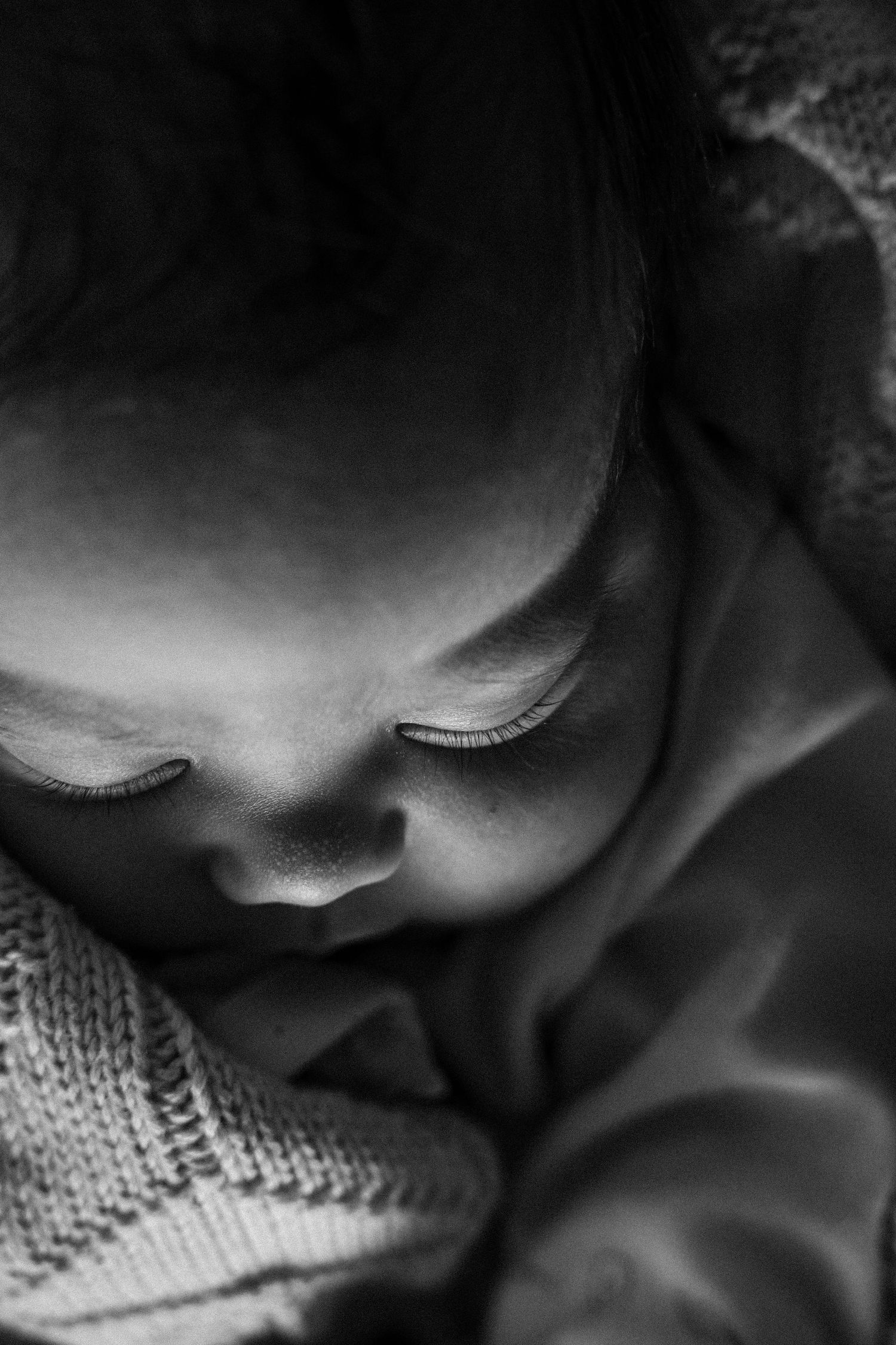 Black and white close-up photo of a sleeping newborn baby wrapped in a soft knit blanket.