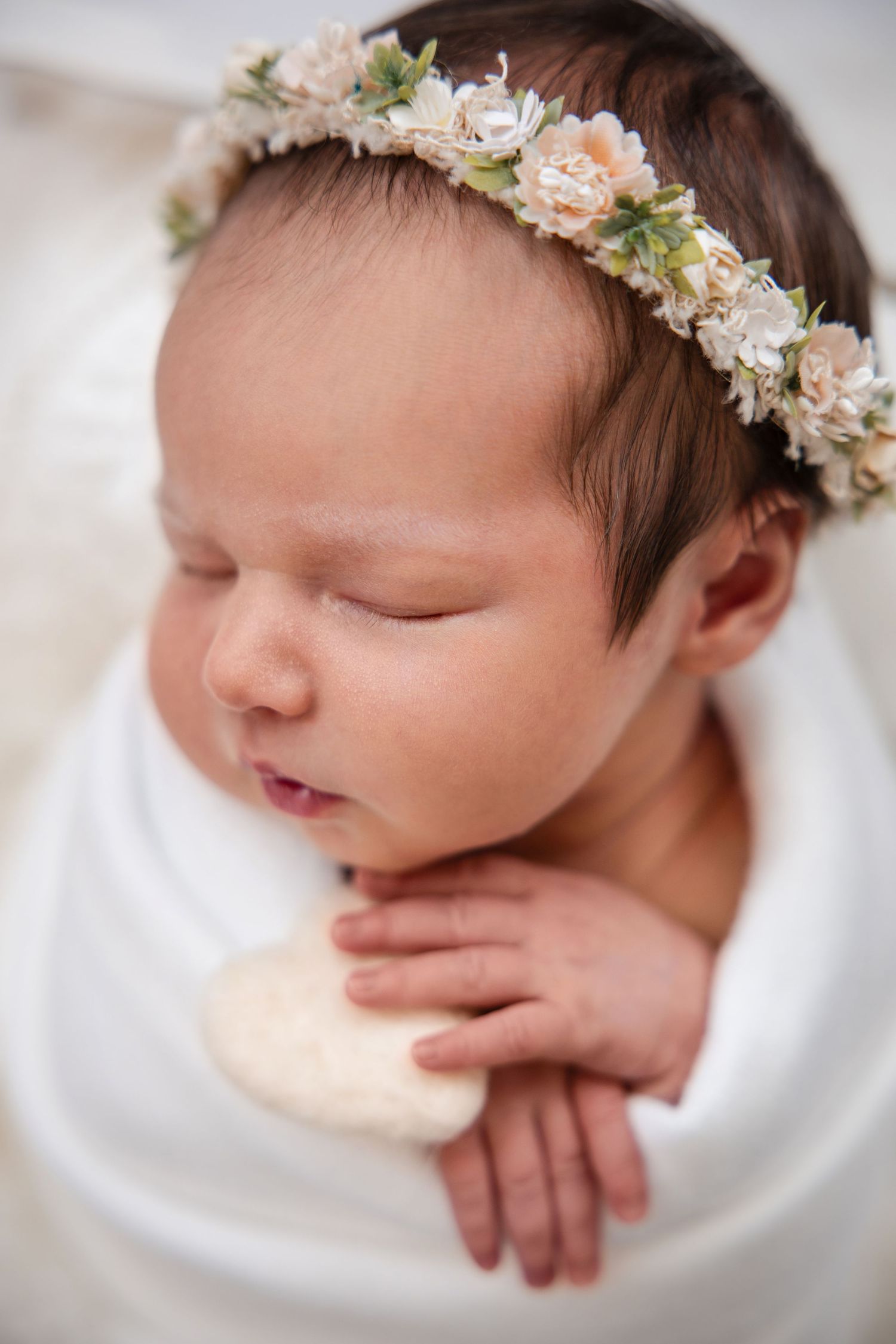 Sleeping newborn baby wearing delicate peach and white floral crown in soft white studio portrait series.