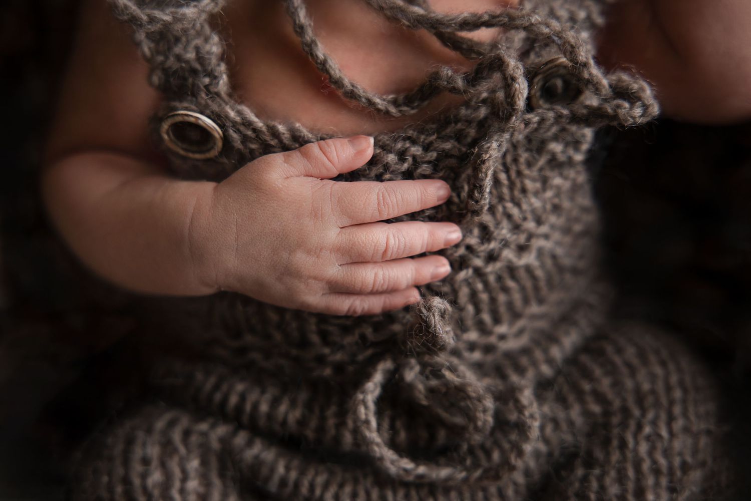 Small hands hold a cozy knitted gray blanket in a moody dark setting.