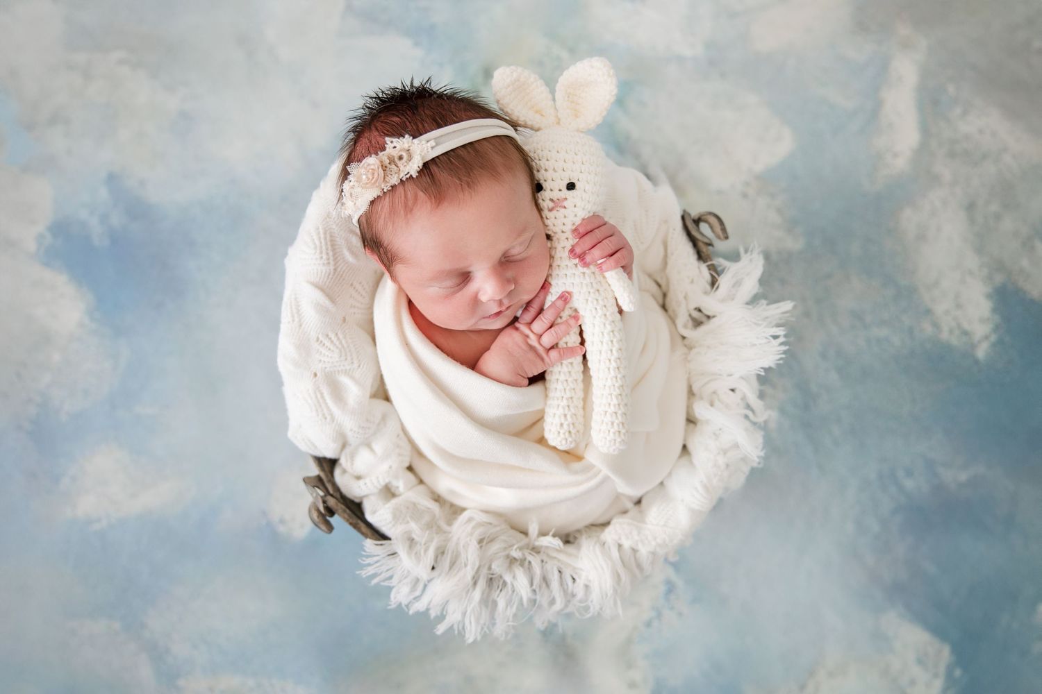 A series of dreamy newborn portraits against a soft cloudy blue background with delicate white wrapping.
