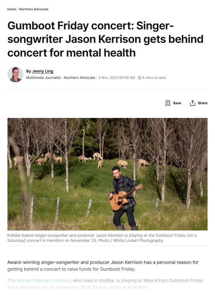 A person performs with an acoustic guitar in an outdoor setting with birch trees in the background.