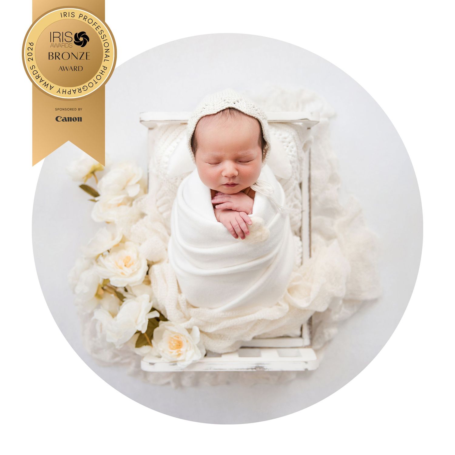 Award-winning newborn photo of a swaddled baby in white wrap, nestled in a vintage white wooden bed with cream flowers.