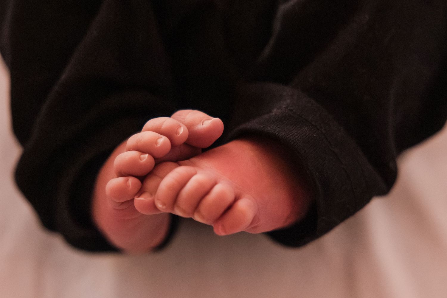 Close-up of tiny newborn baby feet and toes wrapped in a soft black blanket.