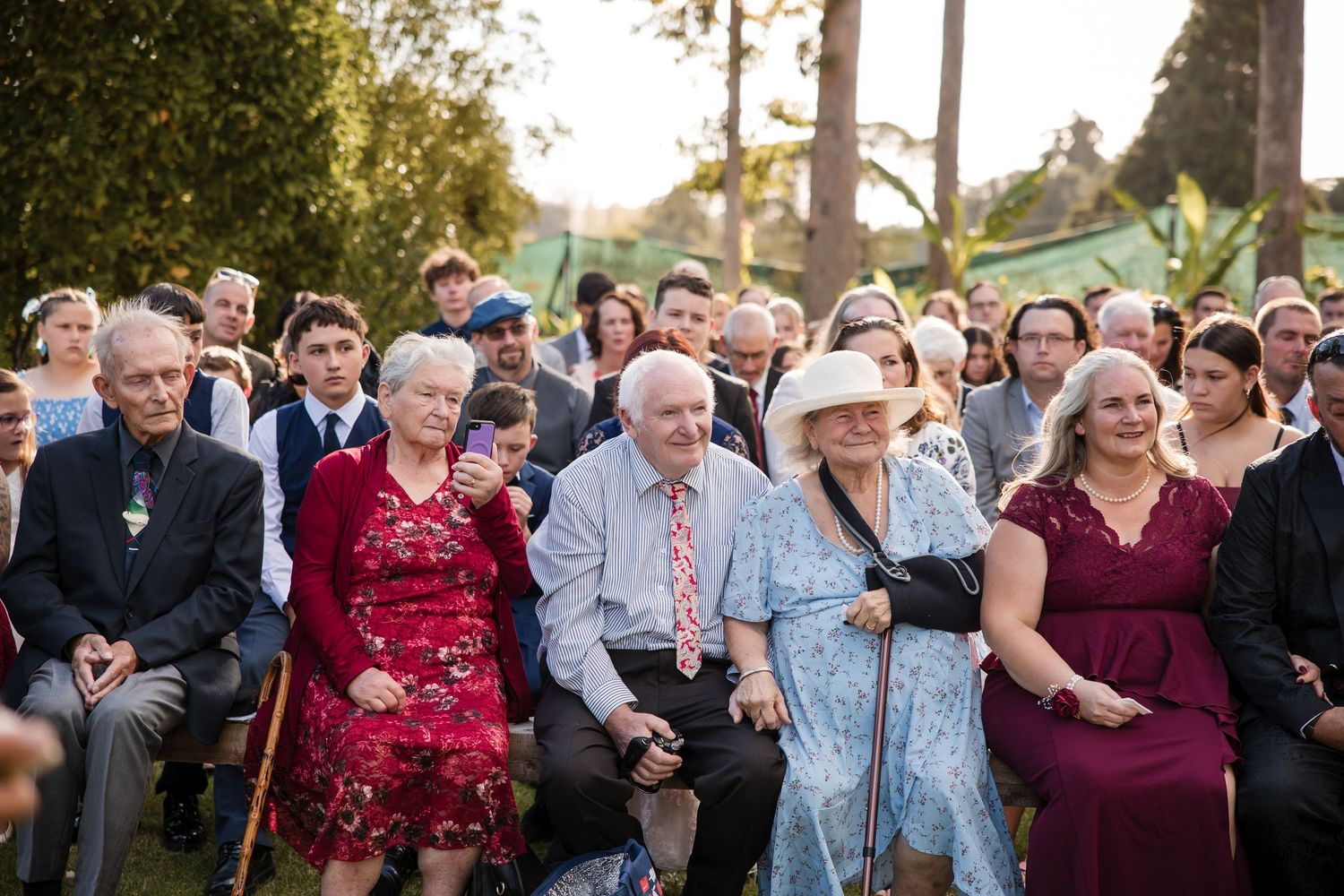 Wedding guests seated outdoors laughing and smiling during an evening garden ceremony.