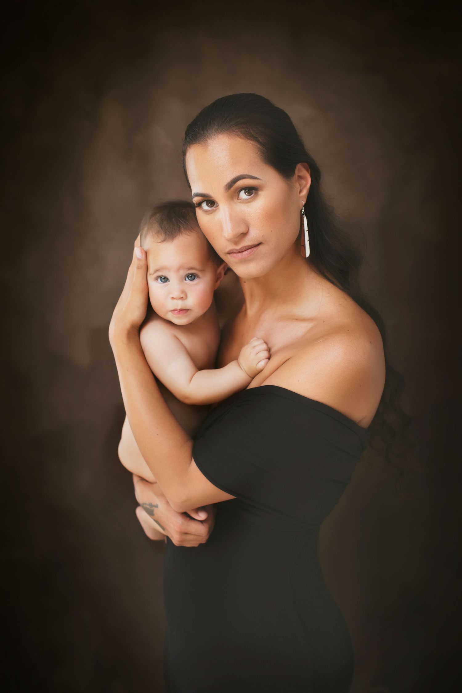 Elegant studio portrait of mother in black dress holding baby against dark background. Cambridge Waikato NZ Photographer