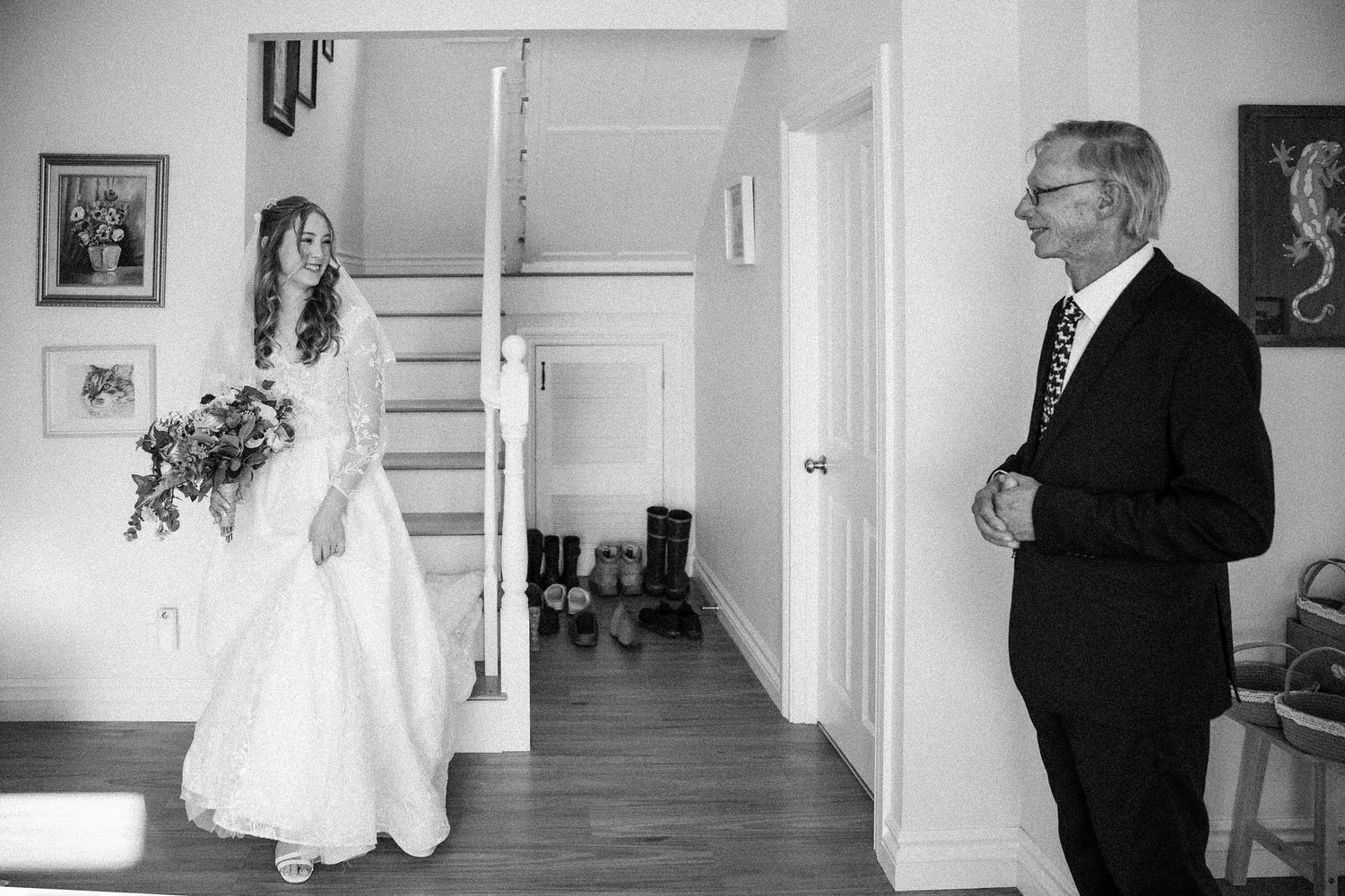 A black and white photograph showing a person in a wedding dress standing in a hallway with someone in a suit.