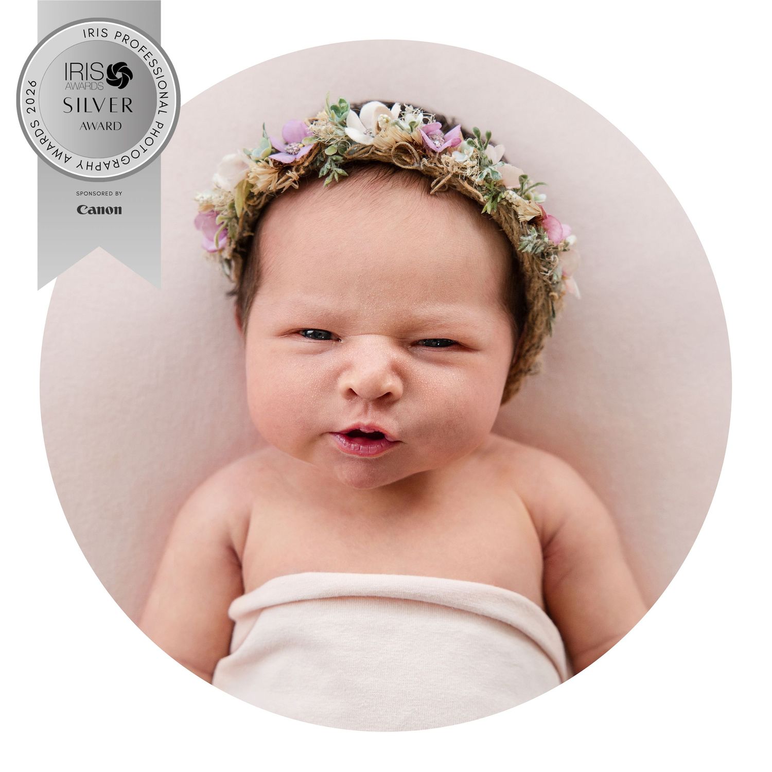 Award-winning newborn portrait of a baby wearing a delicate floral crown, wrapped in soft white fabric.