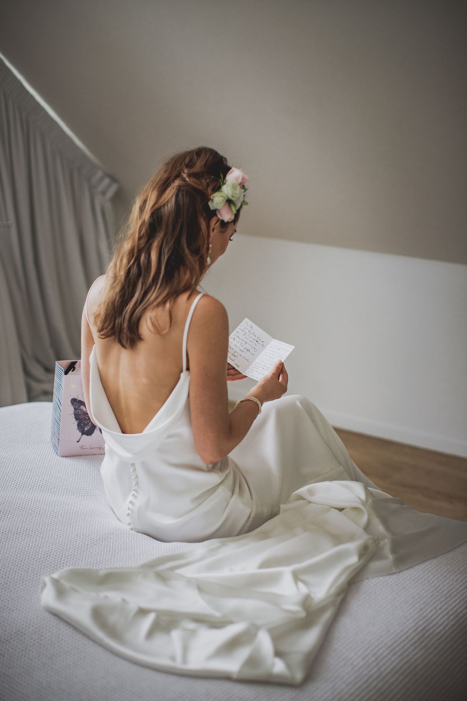 Bride in white dress with flowers in hair reading on bed during wedding preparations. Cambridge Waikato NZ Photographer. White Locket