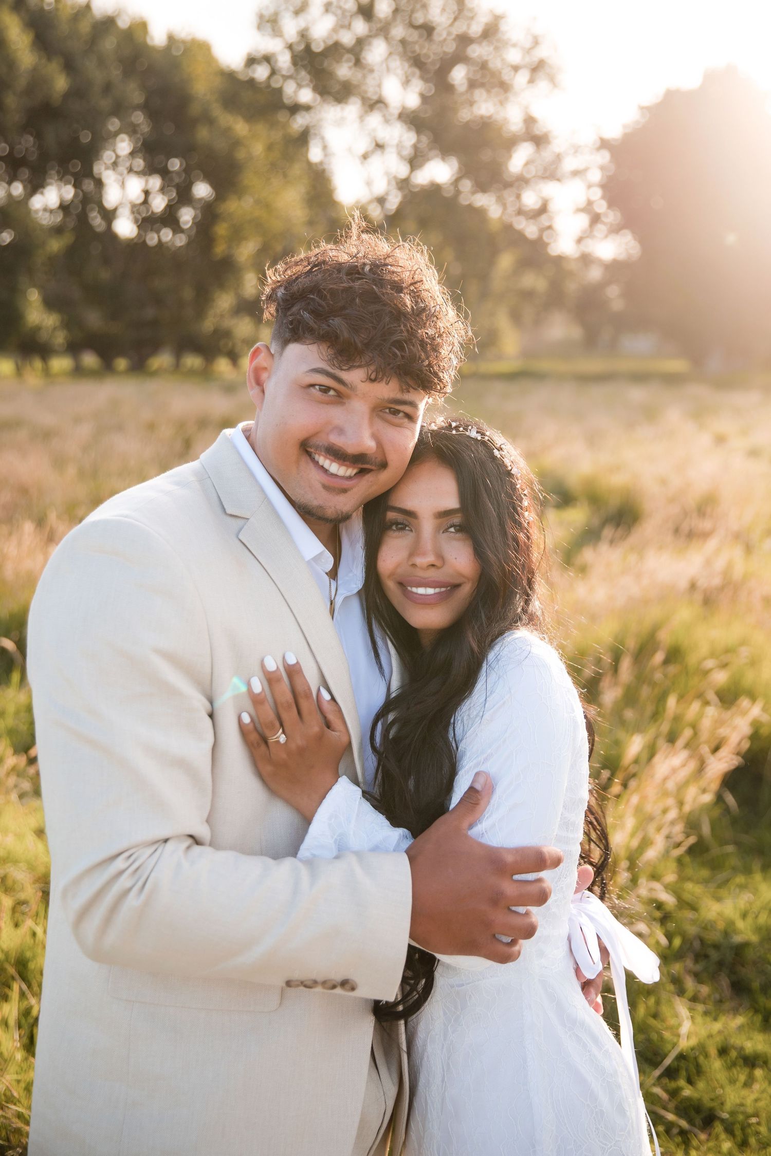A couple embraces joyfully in a sunlit field during their engagement photoshoot at golden hour.
