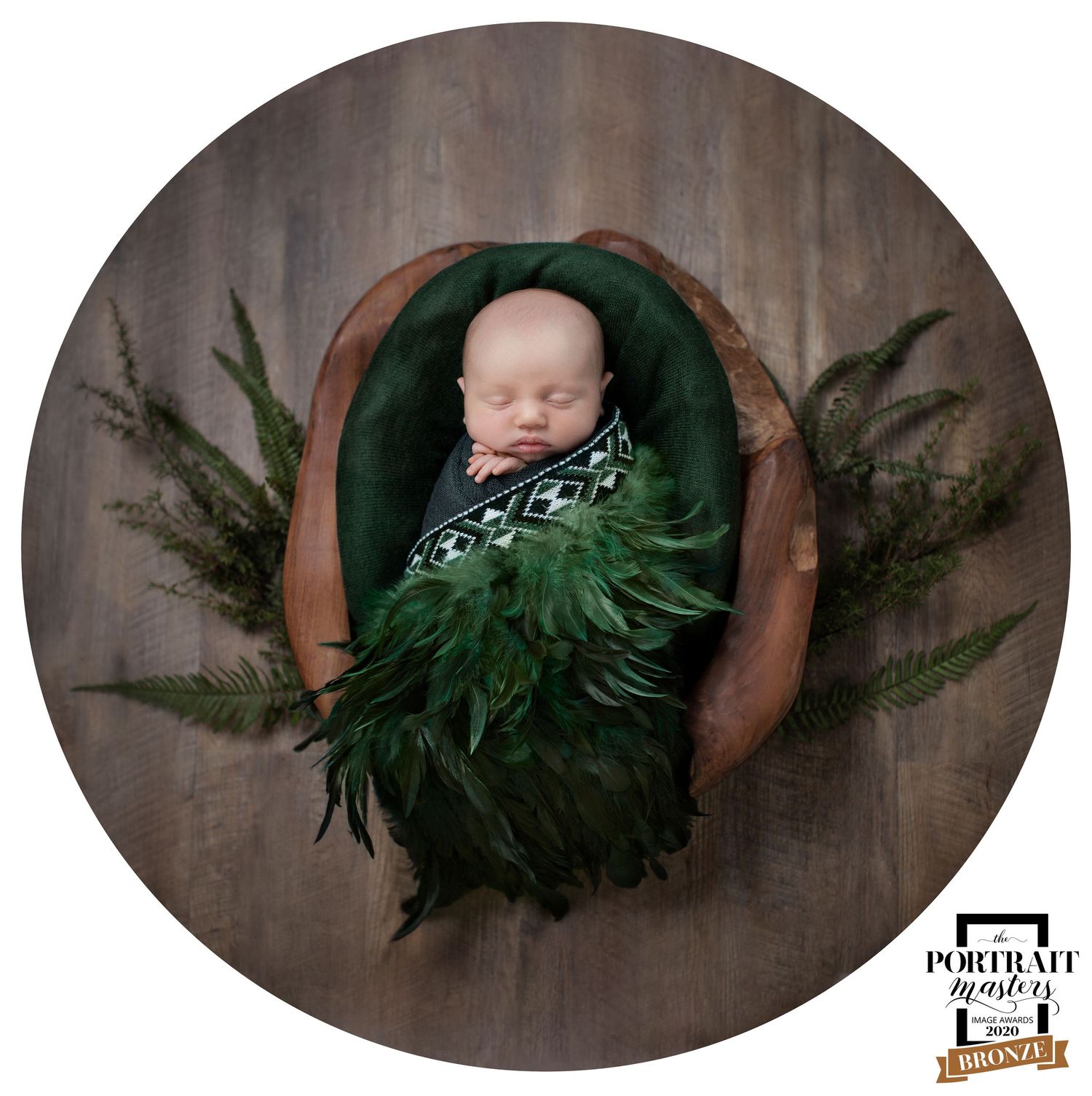 A sleeping newborn rests peacefully on a brown surface surrounded by decorative evergreen branches in a holiday portrait.
