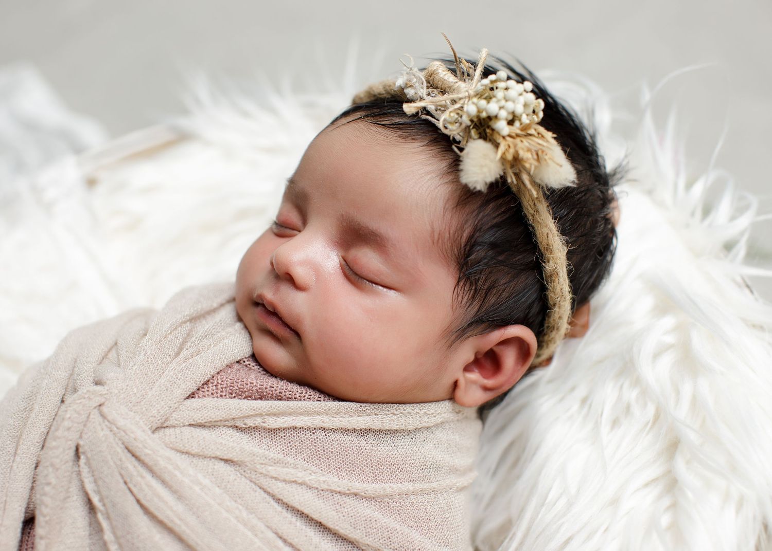 Sleeping newborn wearing gold floral headband swaddled in light fabric on white fur. Cambridge Waikato NZ Photographer