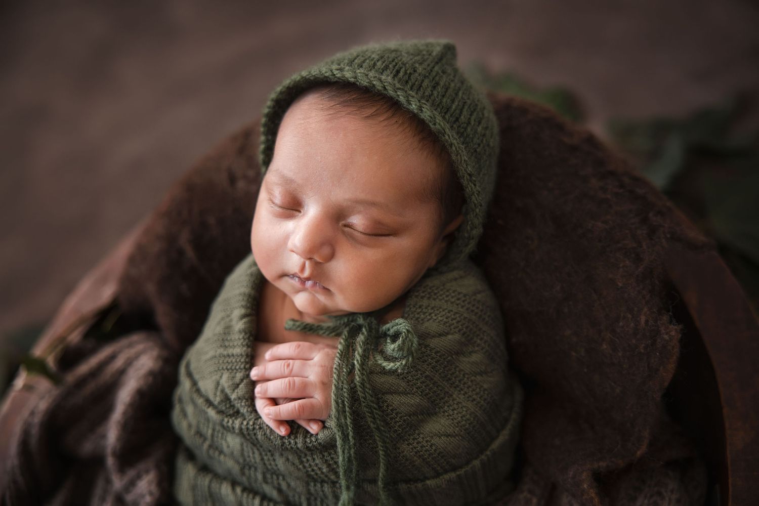 Four tender photos of a sleeping baby wrapped snugly in cozy green knitwear against dark backgrounds.