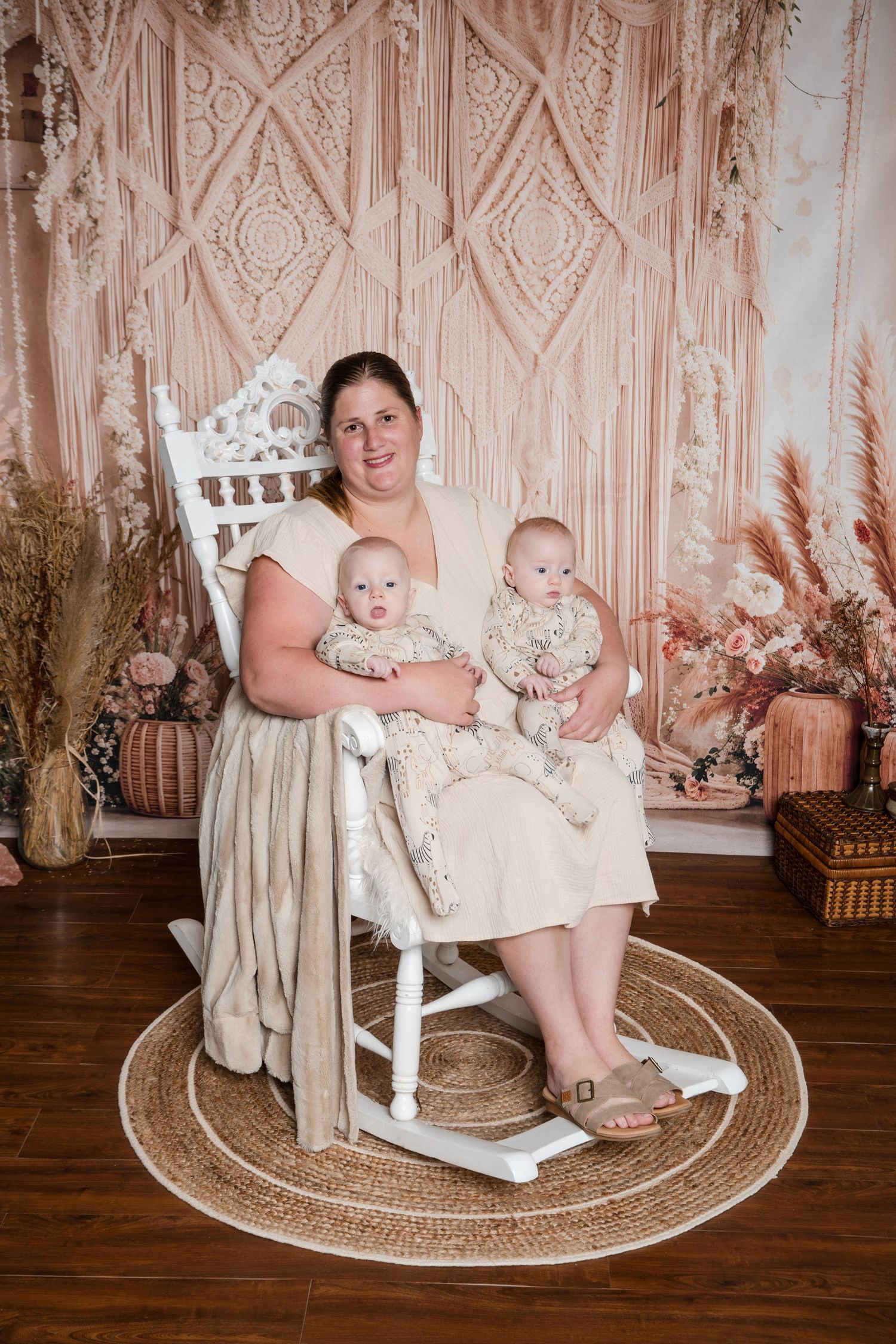 Professional family portrait against beige macrame backdrop with pampas grass decor on round jute rug.