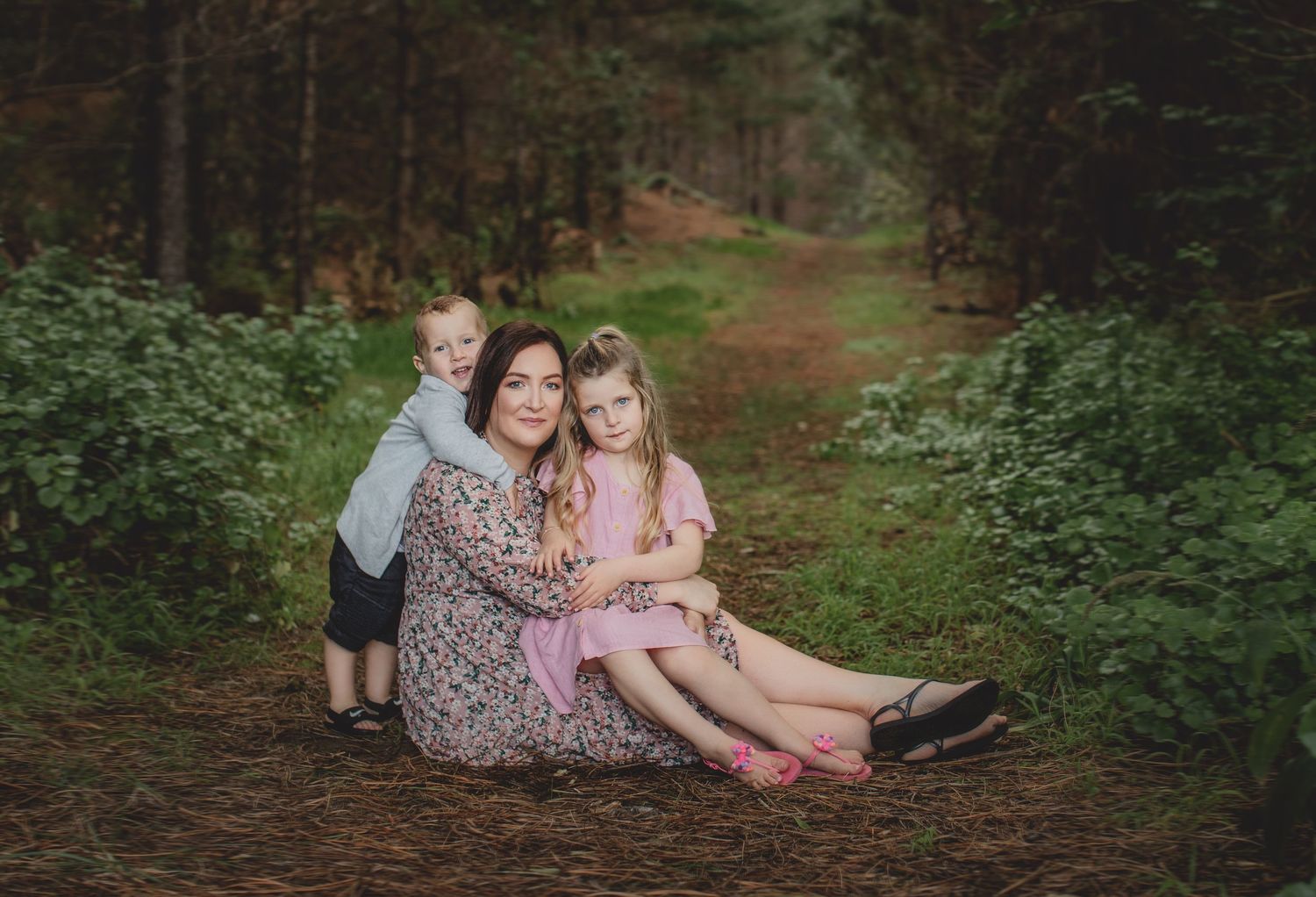 Family sits together on forest path surrounded by lush greenery.