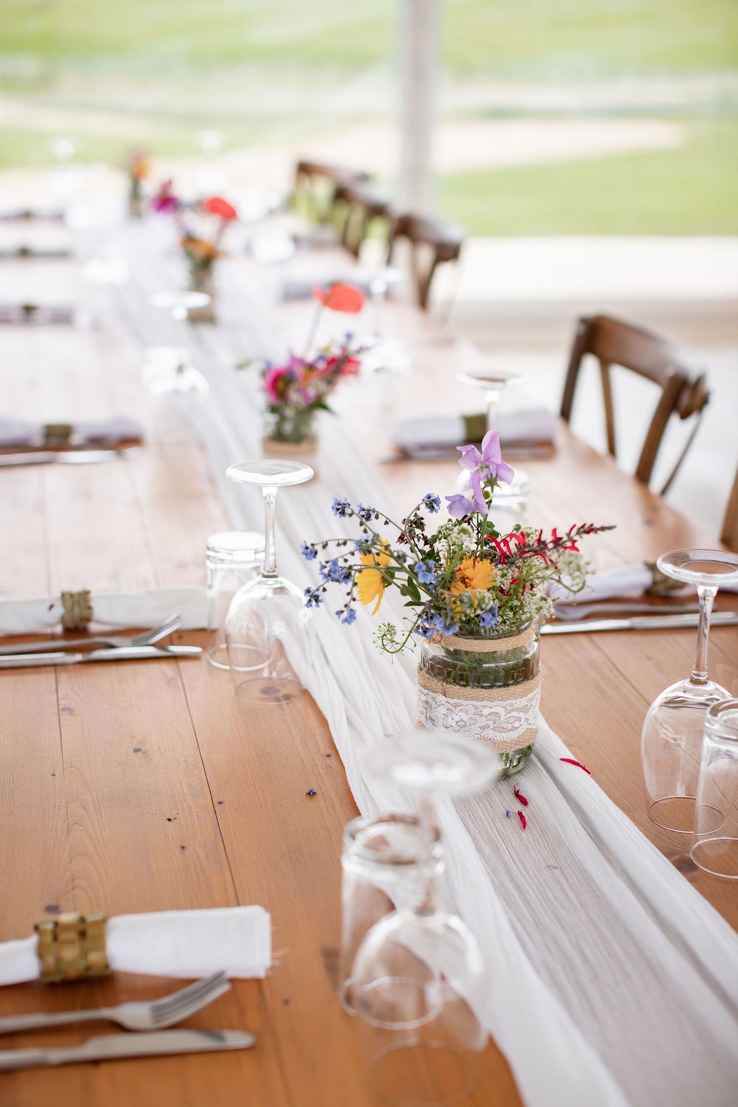 Rustic wedding reception table decorated with wildflower centerpieces in mason jars and white table runner.