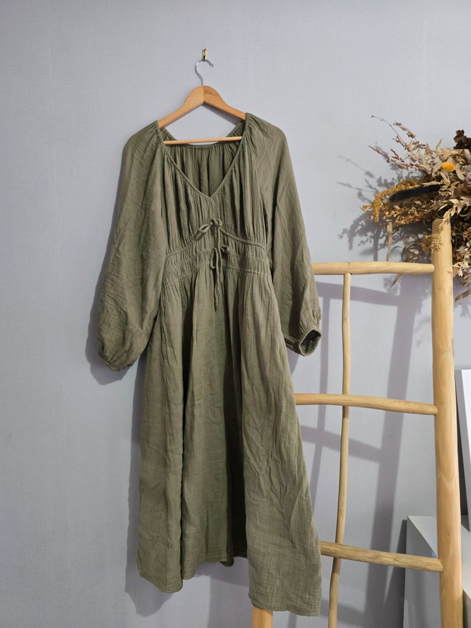 Olive green linen midi dress with V-neck, long balloon sleeves, and drawstring waist, displayed on a wooden hanger.