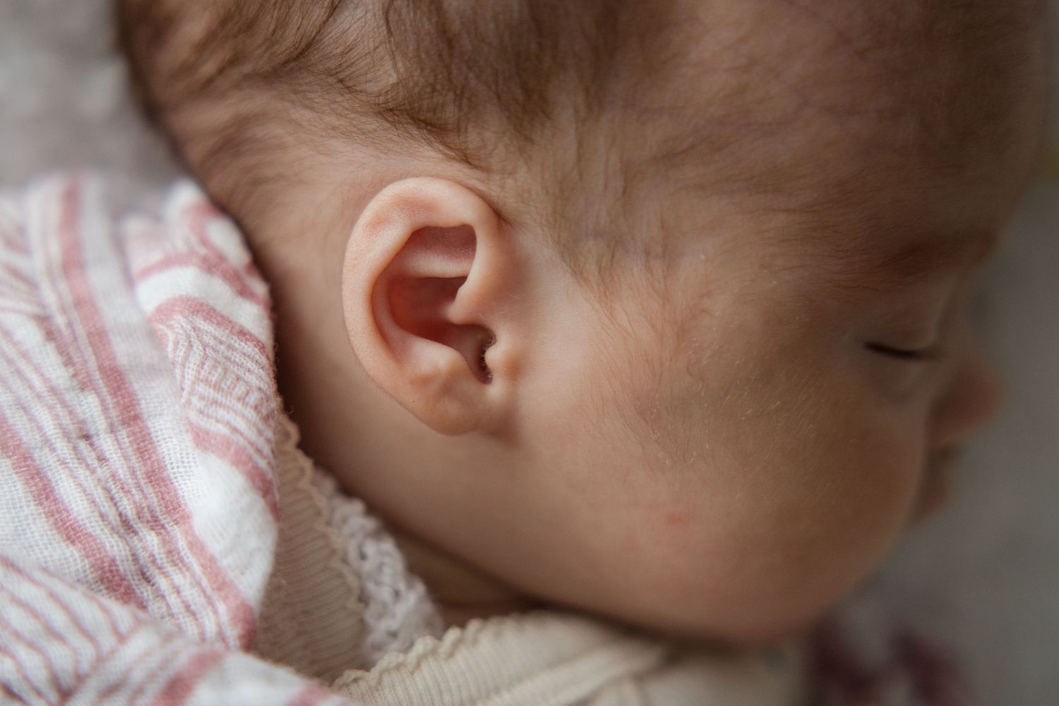 Close-up of peaceful sleeping newborn baby ear and profile wrapped in soft pink striped blanket.