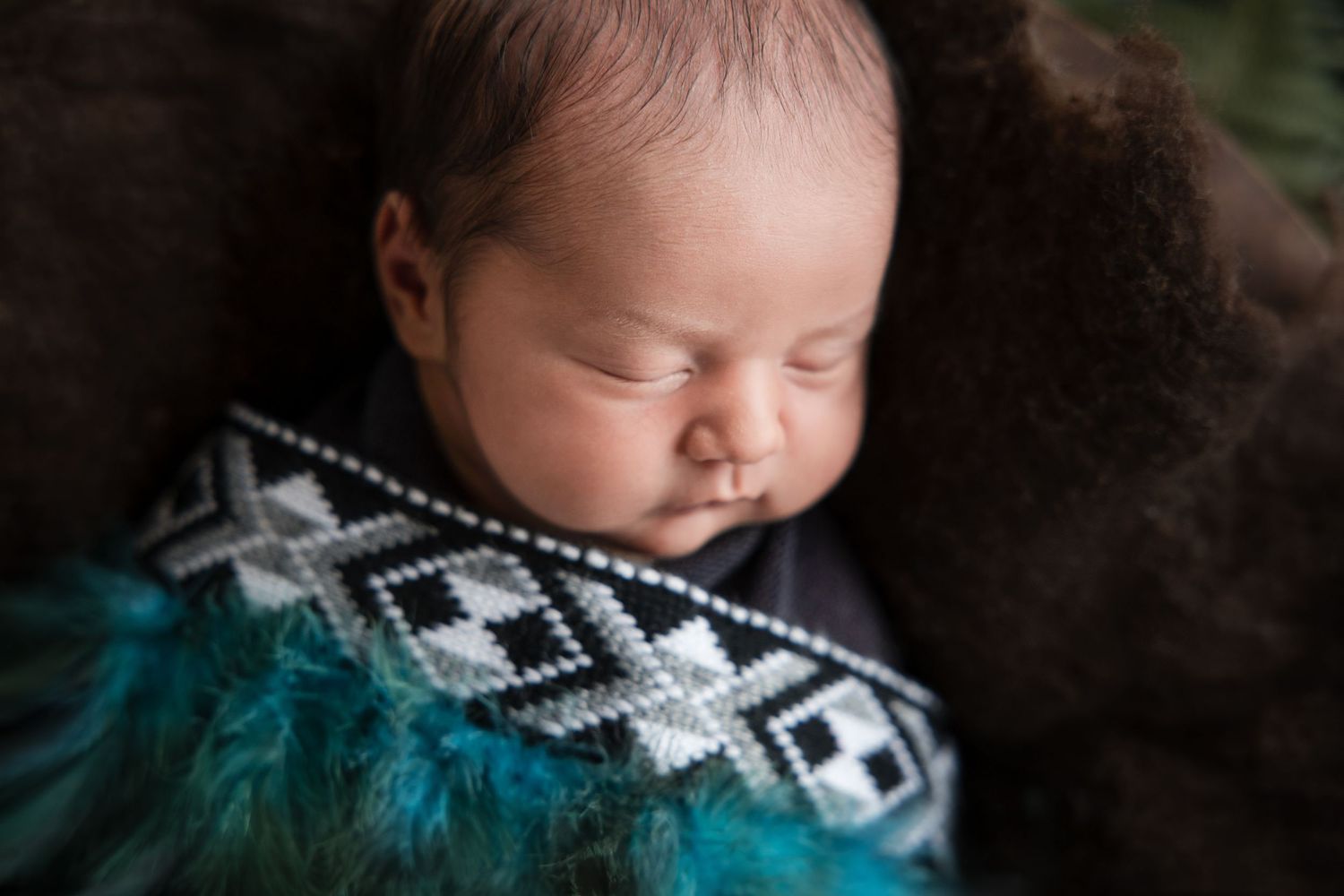 Sleeping baby nestled in patterned blanket with turquoise accents against dark background.