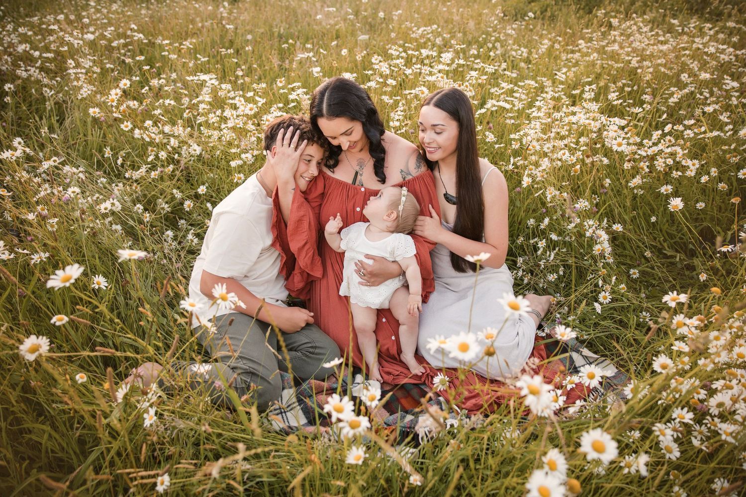 Family with baby sitting in a blooming daisy field, enjoying a warm sunny day outdoors together.