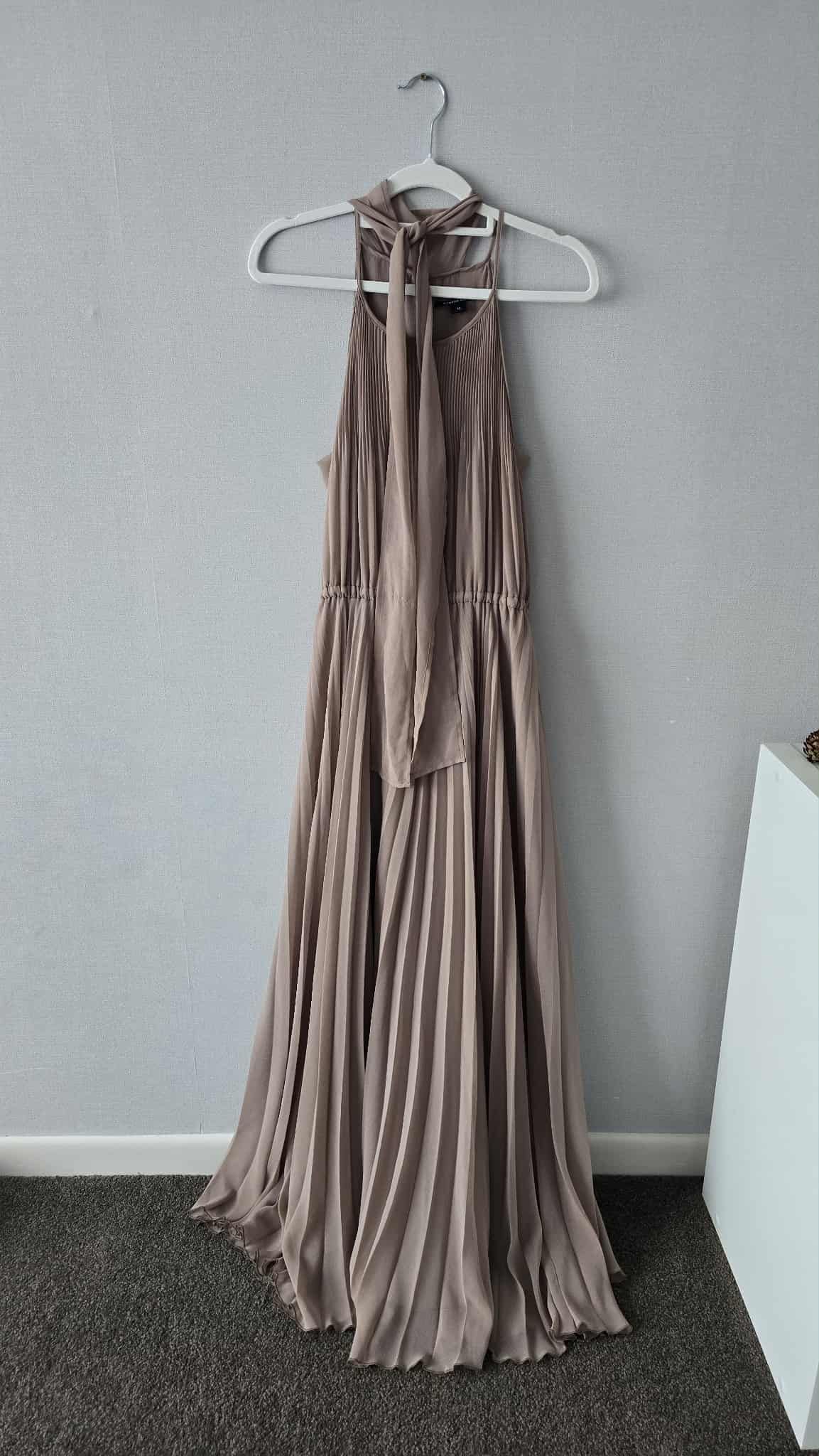 Elegant taupe pleated halter maxi dress on white hanger, featuring a flowing skirt and tie neck detail.