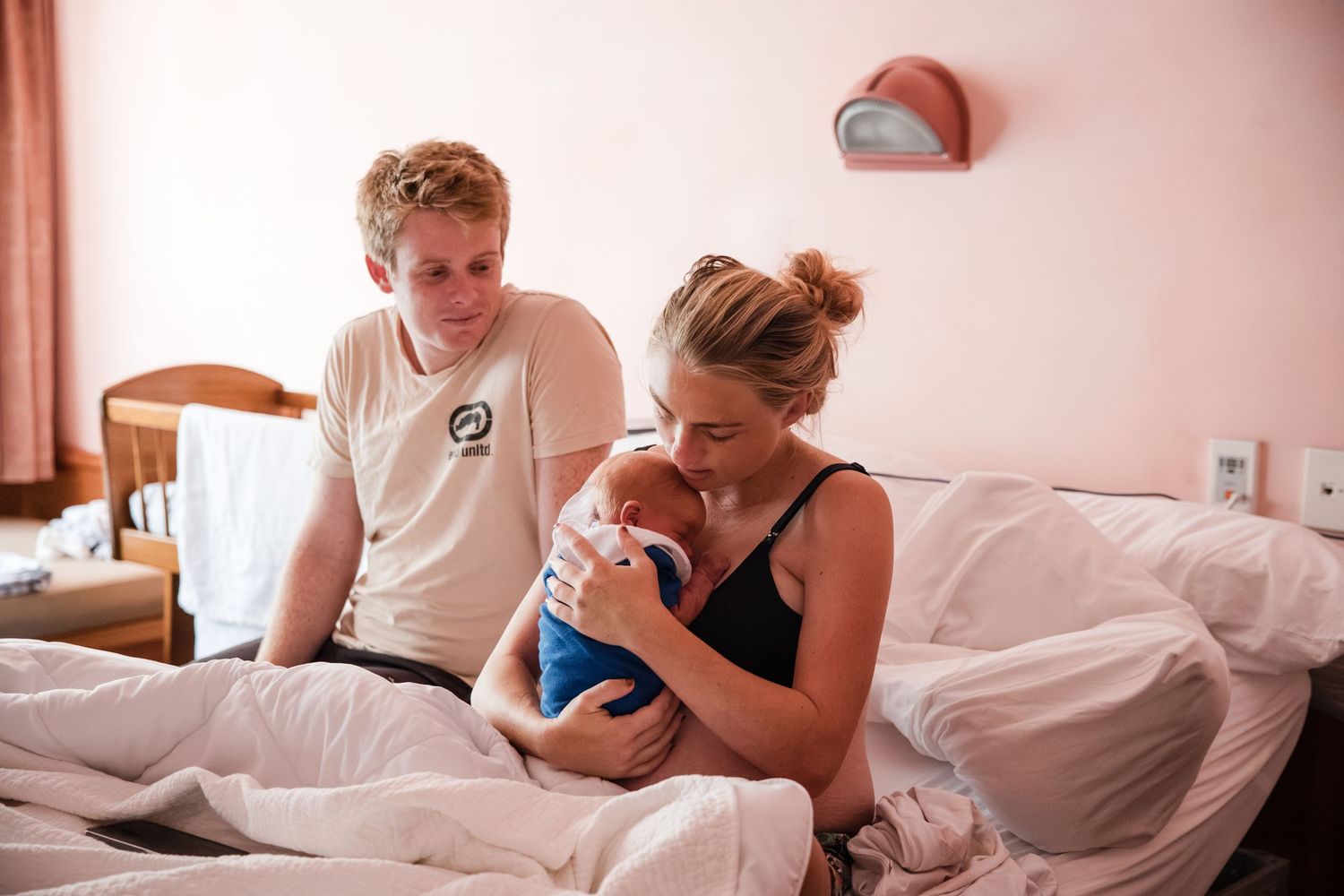 New parents admiring their newborn baby in a hospital room, mother holding infant while father sits beside her.