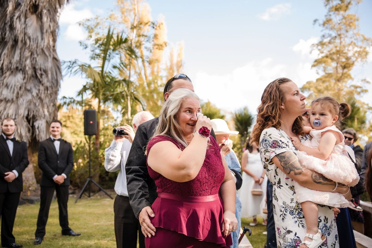 Wedding guests celebrate and dance together during an outdoor reception with palm trees in the background.