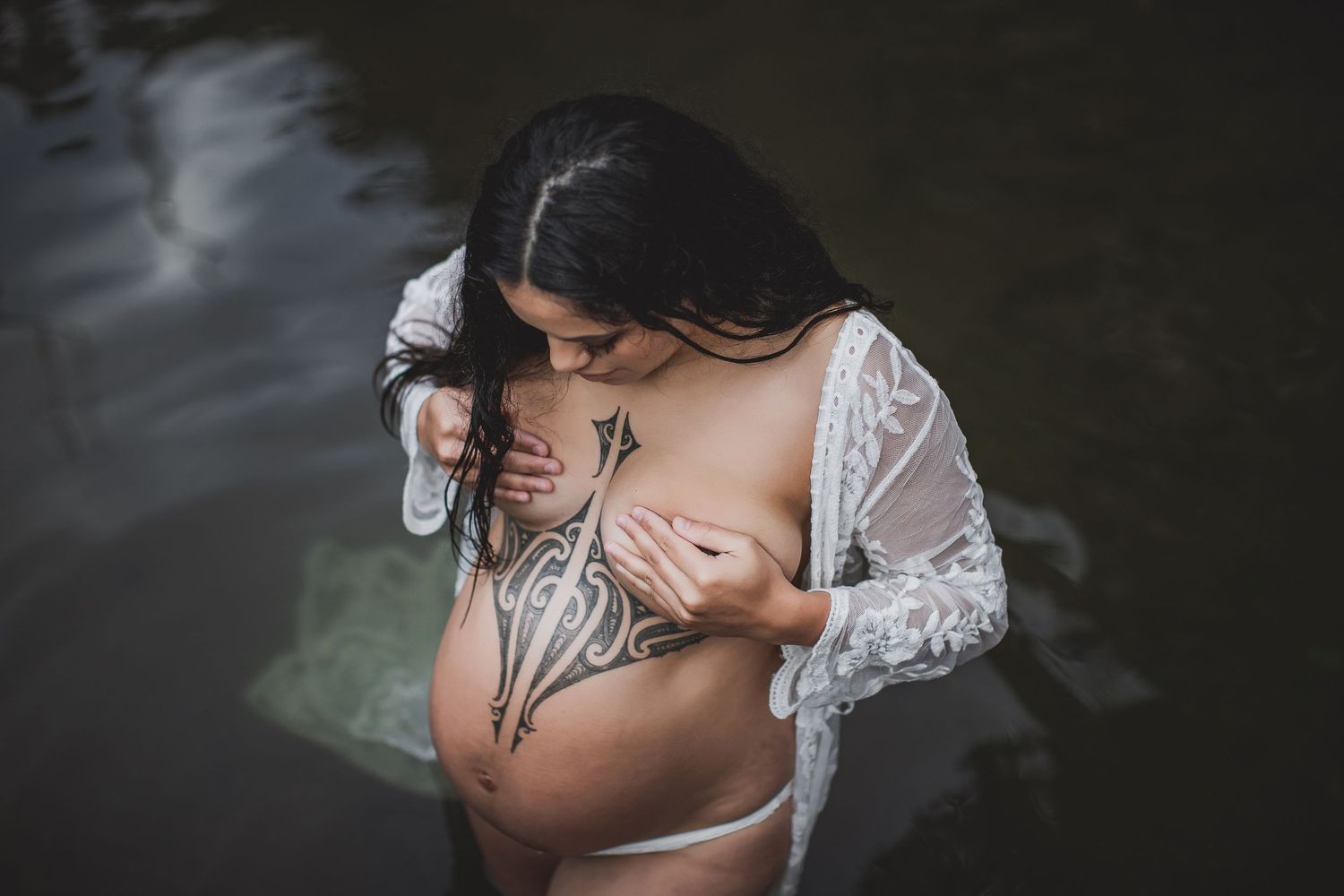 Intimate maternity portrait in water featuring delicate lace and artistic body paint designs.