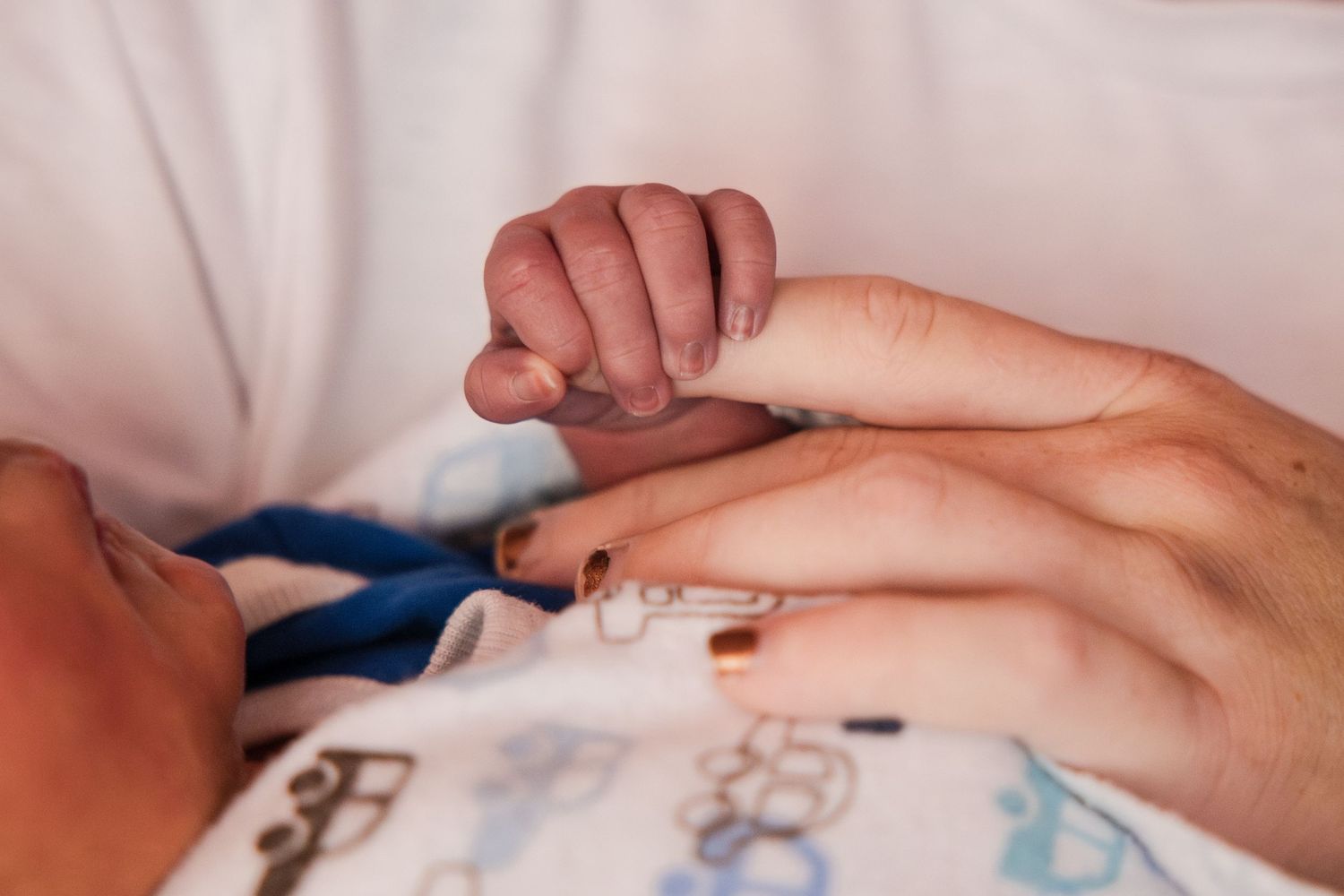 Newborn baby grasping adult finger, close-up of tiny infant hand holding parent's finger gently.
