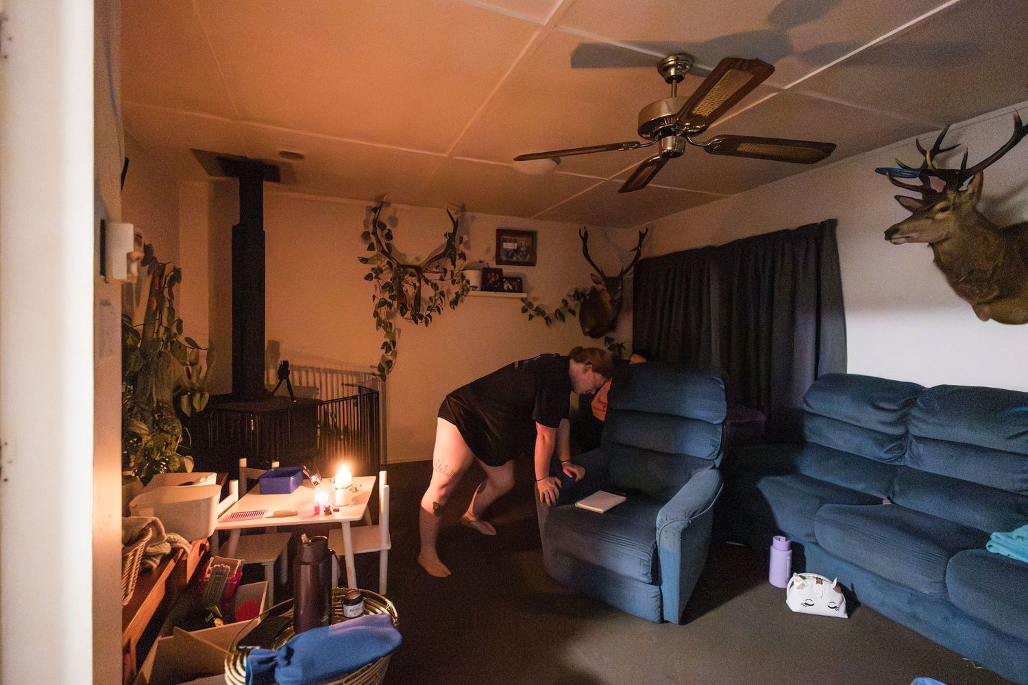 A dimly lit living room with mounted deer heads on the wall, a ceiling fan, and a blue sectional couch.
