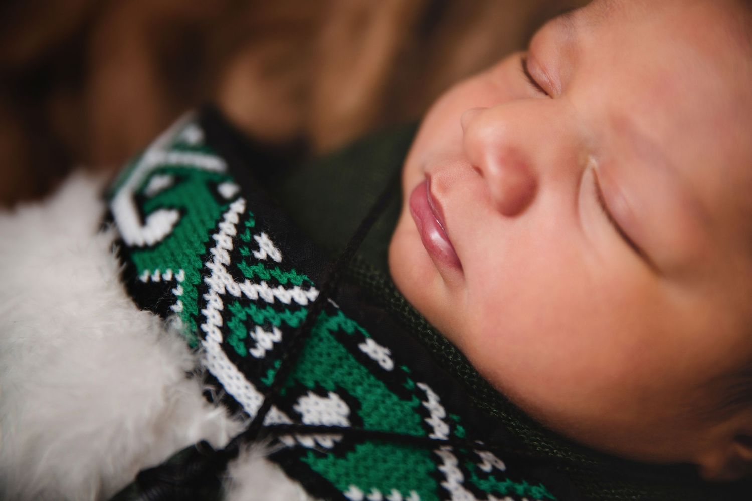 Close-up of peaceful sleeping baby in green Fair Isle sweater with white trim.