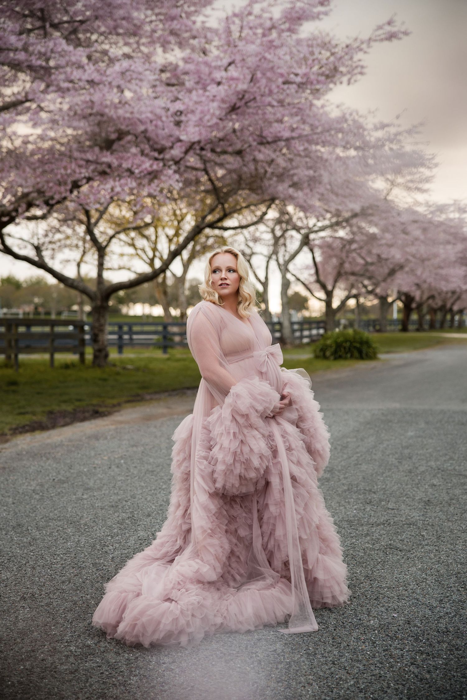 Cherry blossom trees frame a path where someone poses in a flowing pink tulle gown.