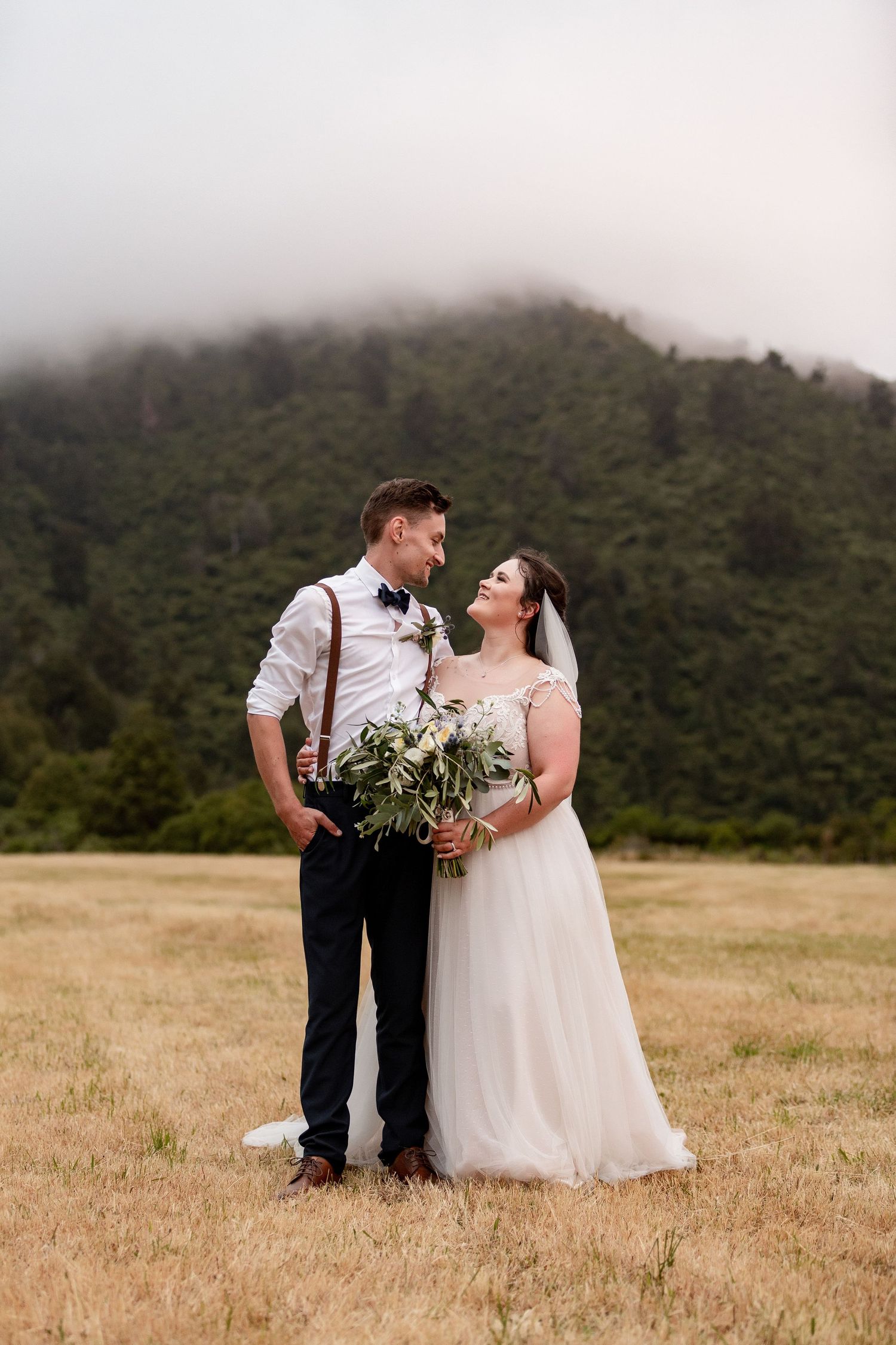 Newlyweds share intimate moment in mountain field with foggy peaks behind them. Cambridge Waikato NZ Photographer. White Locket Photography