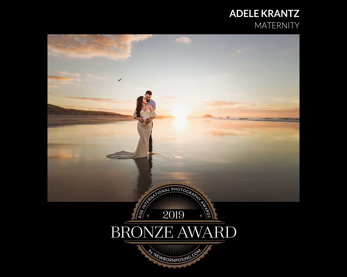 A couple embraces on a reflective beach at sunset with a bronze award emblem displayed below.