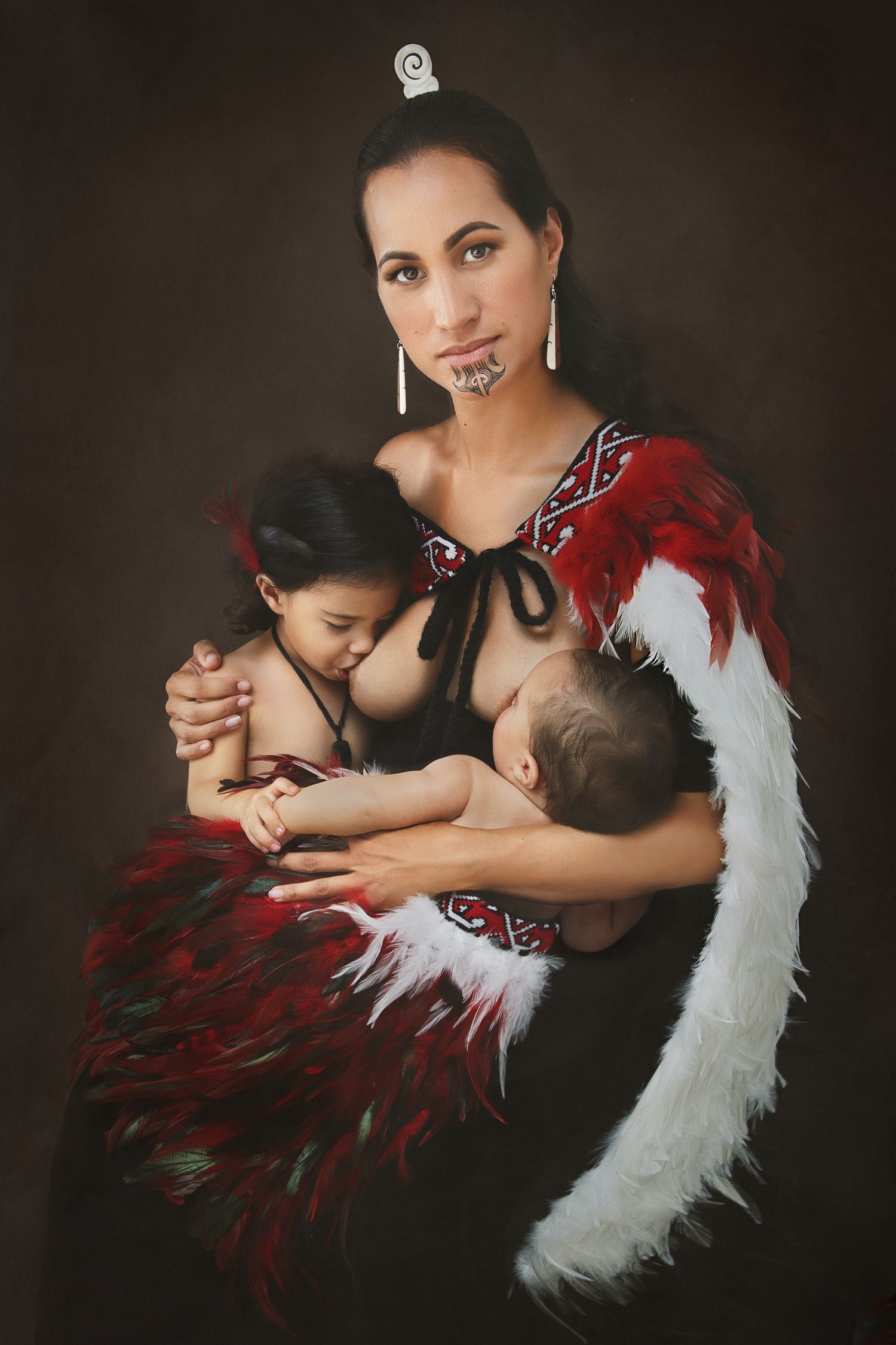 Traditional Maori breastfeeding portrait with woman wearing red feathered cloak nursing two babies. Cambridge Waikato NZ Photographer