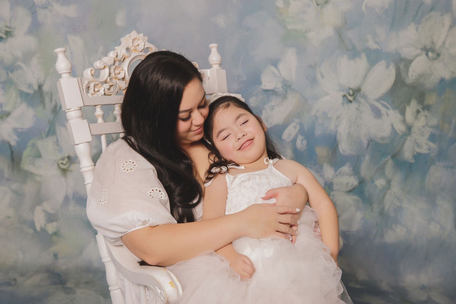 A tender moment captured against a dreamy floral backdrop, showing warmth and connection in matching white dresses.