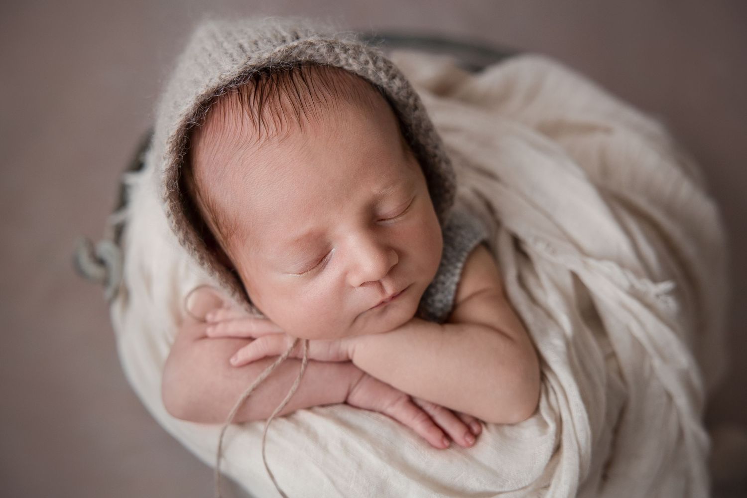A sleeping newborn baby wrapped in soft white fabric lies peacefully in a natural light setting.