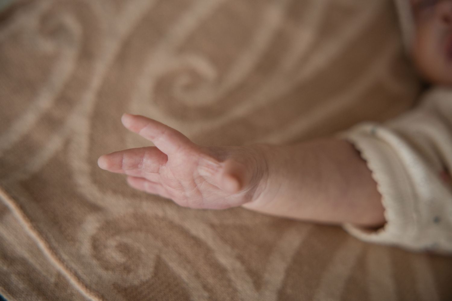 Close-up of a newborn baby's tiny open hand resting on a soft beige patterned blanket.