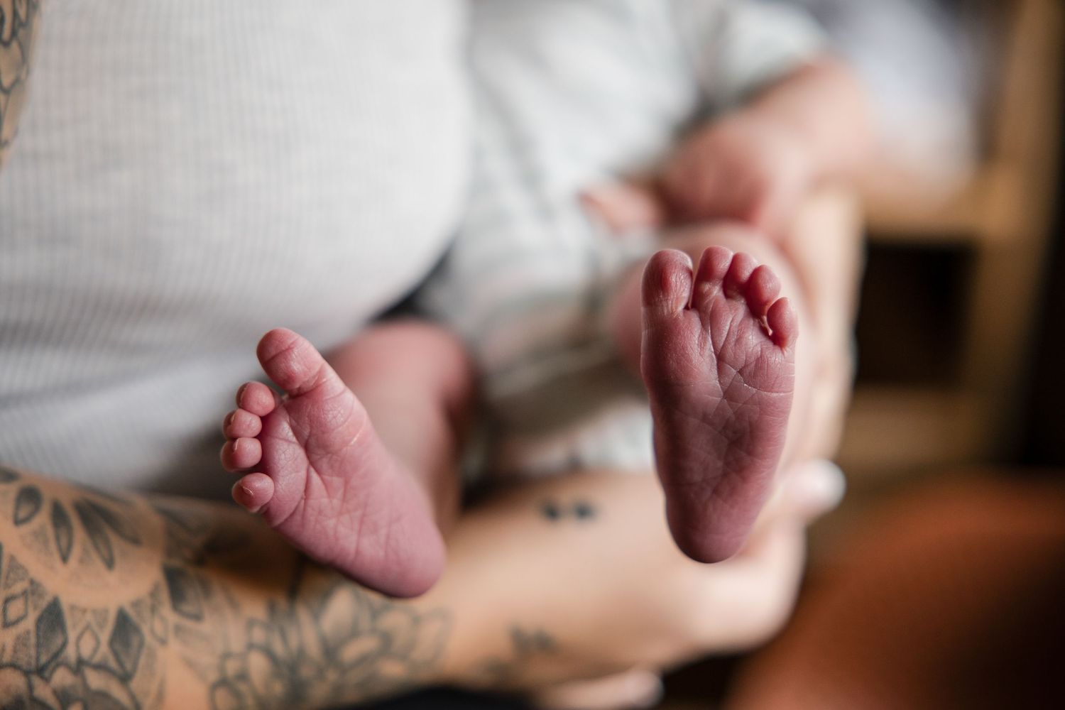 Close-up of tiny newborn baby feet held by a tattooed parent, capturing a tender moment of new parenthood.