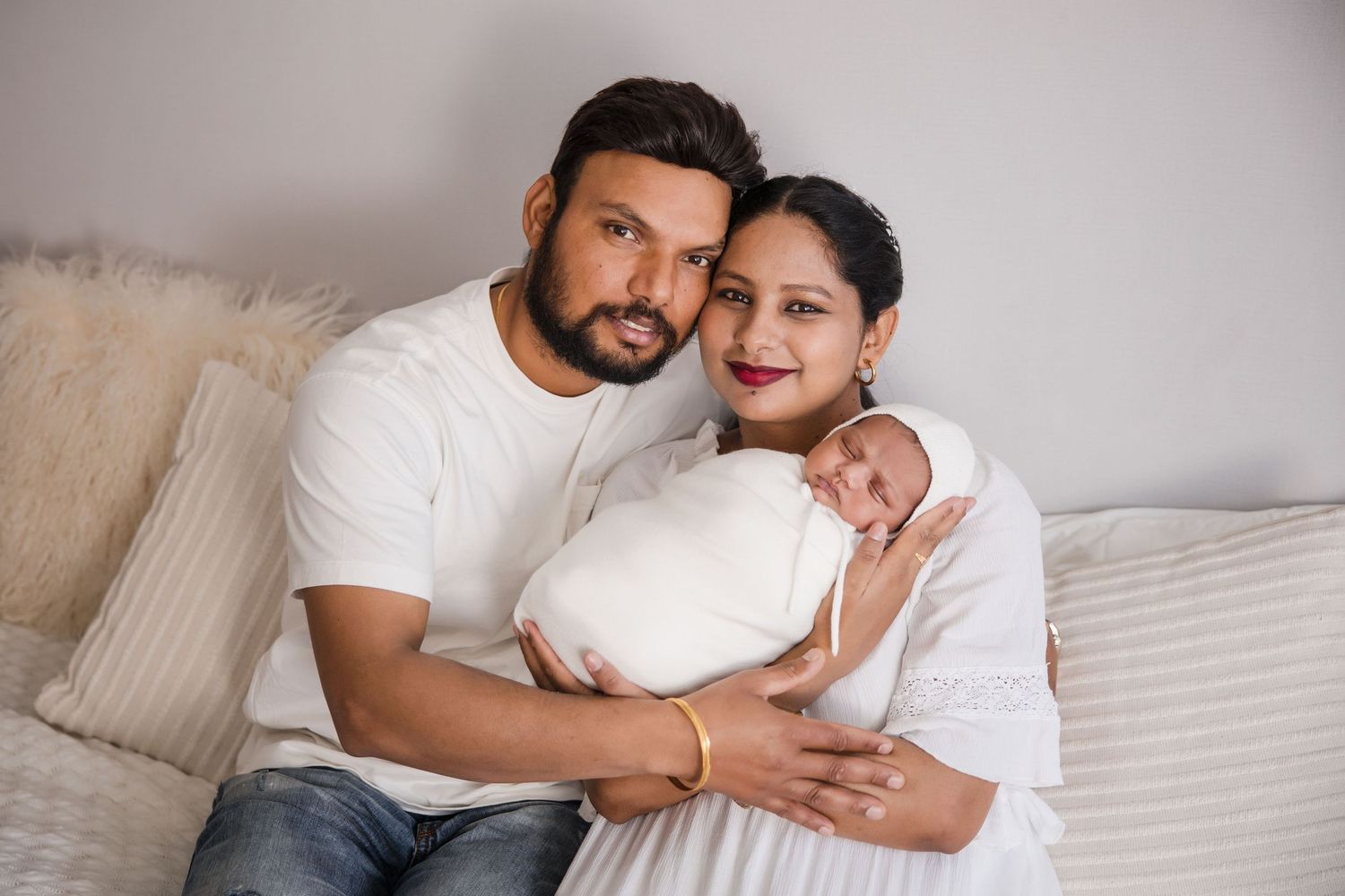 Two people in white shirts embrace lovingly on a couch in a bright, minimalist living room setting.